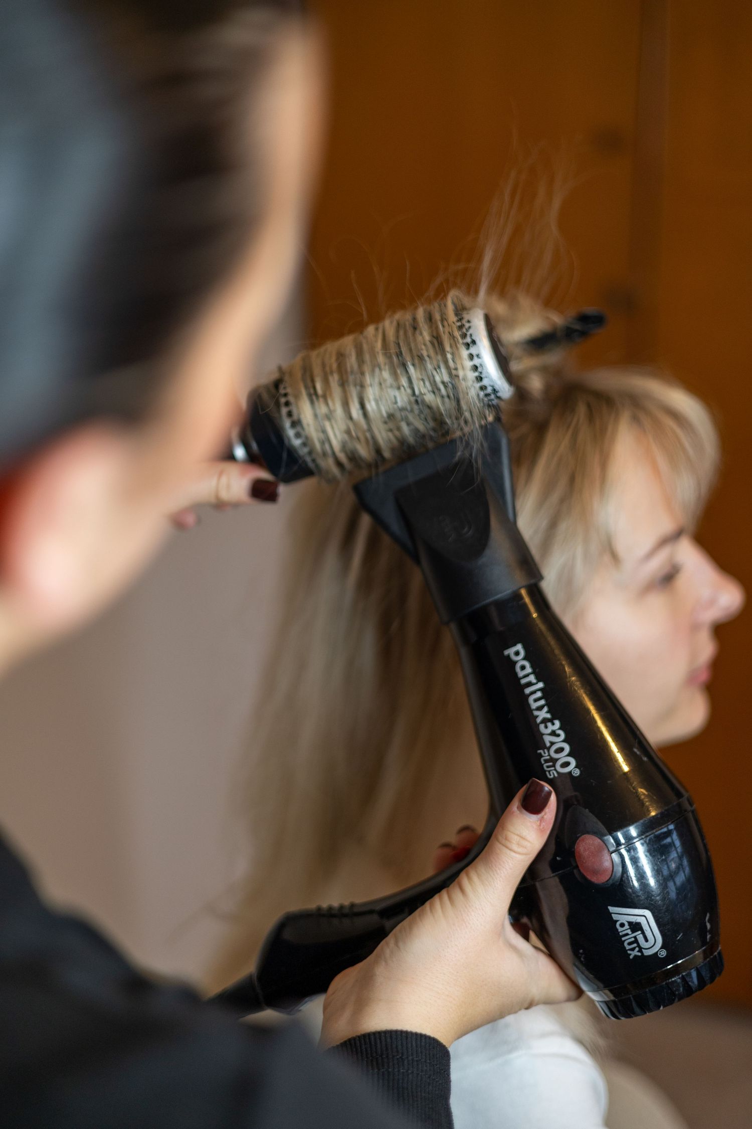 Hairstylist using Parlux 3000 blow dryer and round brush to style blonde woman's hair. South London