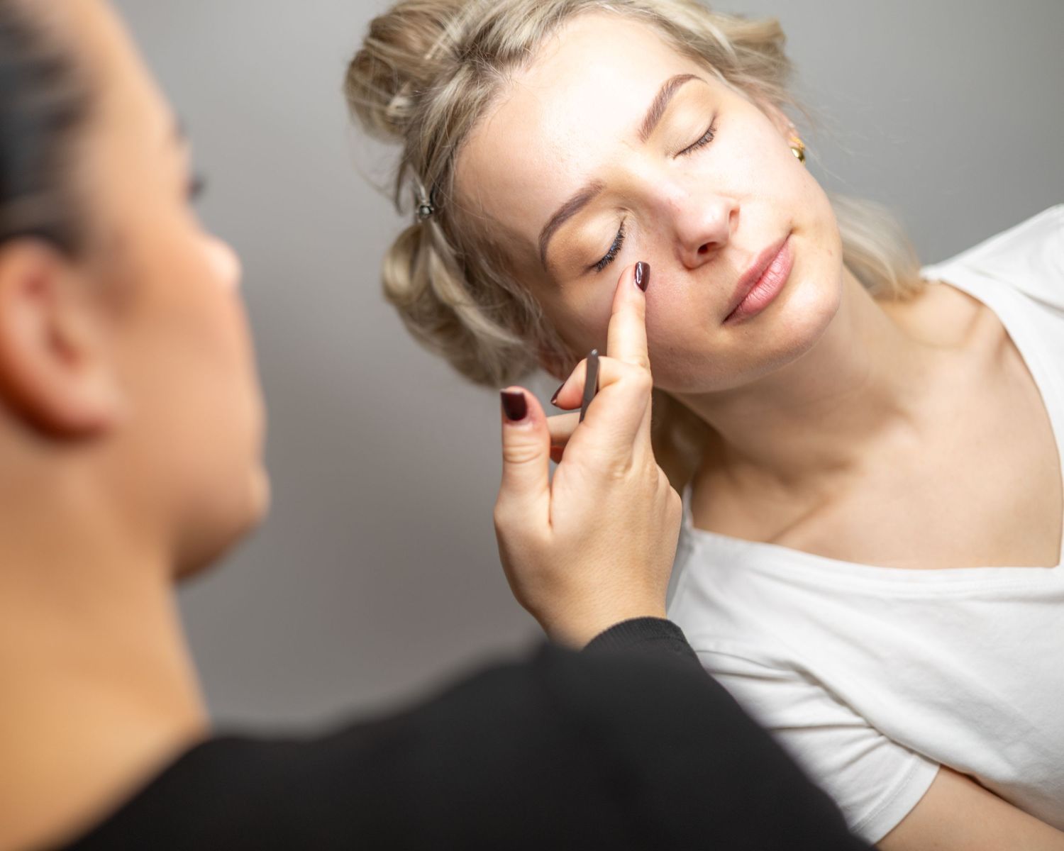 Makeup artist applying foundation to a young blonde woman's face in a professional beauty studio setting. Brand Photography South London
