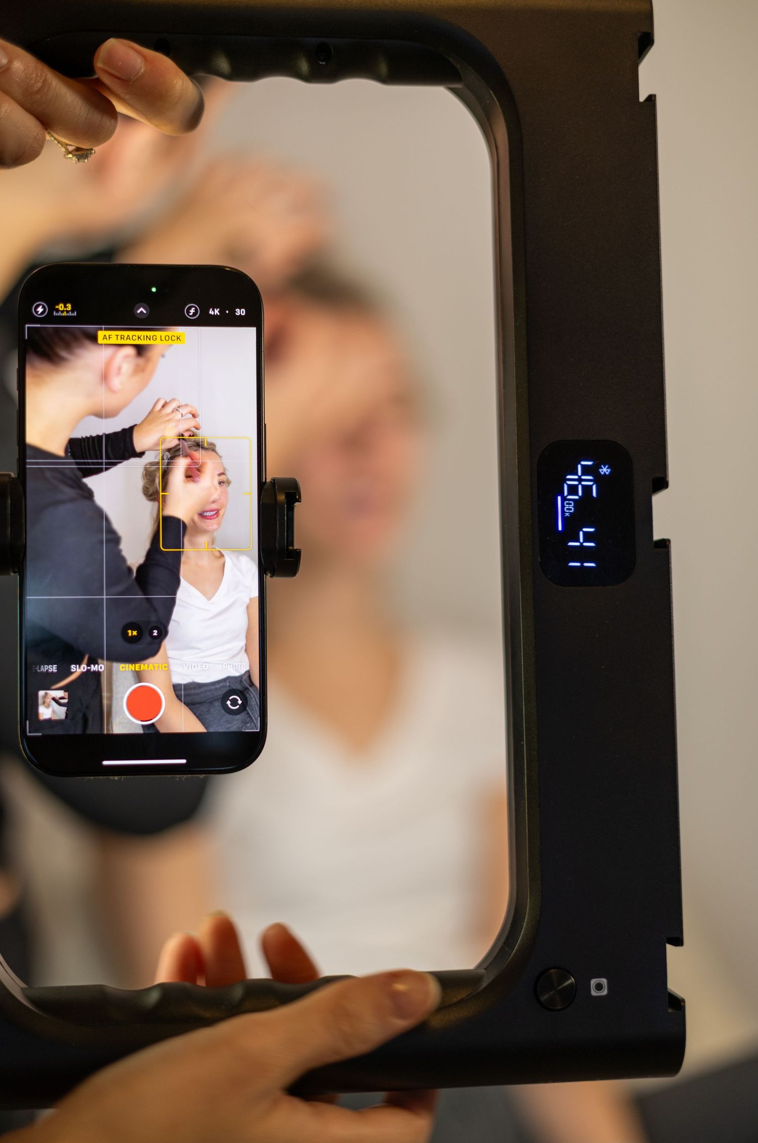 Smartphone on ring light filming makeup artist applying product to blonde woman's hair in studio. South London