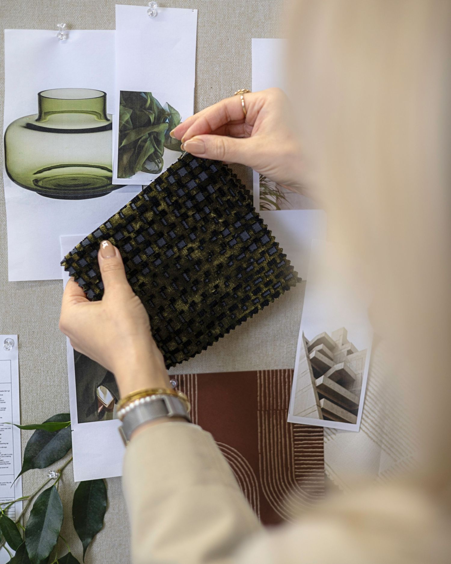 Interior designer examining a dark green woven fabric swatch on a mood board with decor sketches. Brand Photography South London