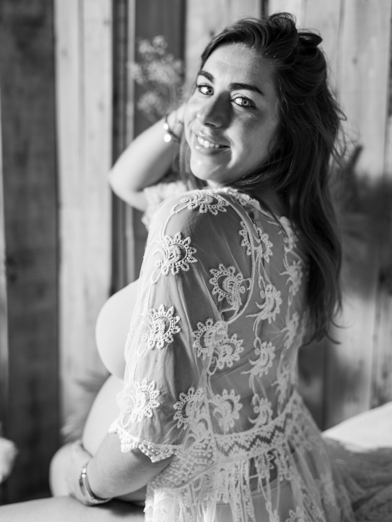 Black and white portrait of a smiling woman in a lace dress looking over her shoulder by a window. Blanes, Spain