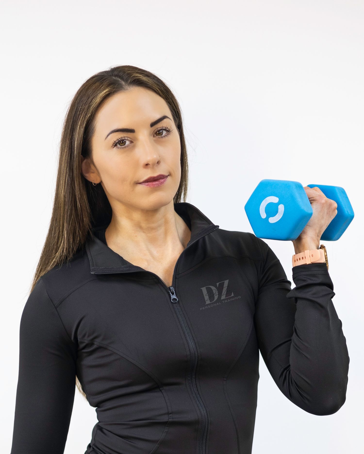 Fit woman in black DZ zip-up jacket holding blue hexagonal dumbbell in professional fitness photo. Personal Trainer in south london