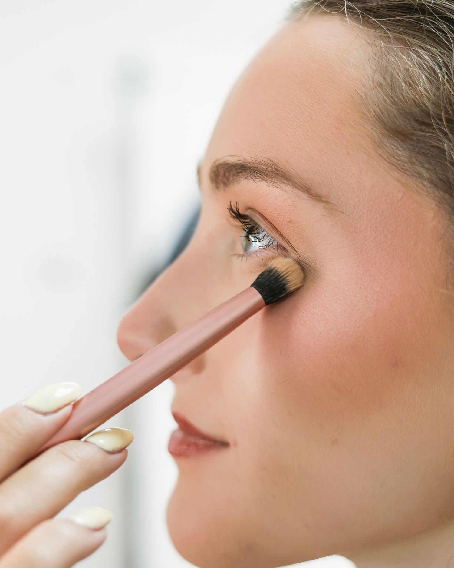 Close-up of makeup artist applying eyeshadow with brush to woman's eye in beauty studio. Brand Photography South London