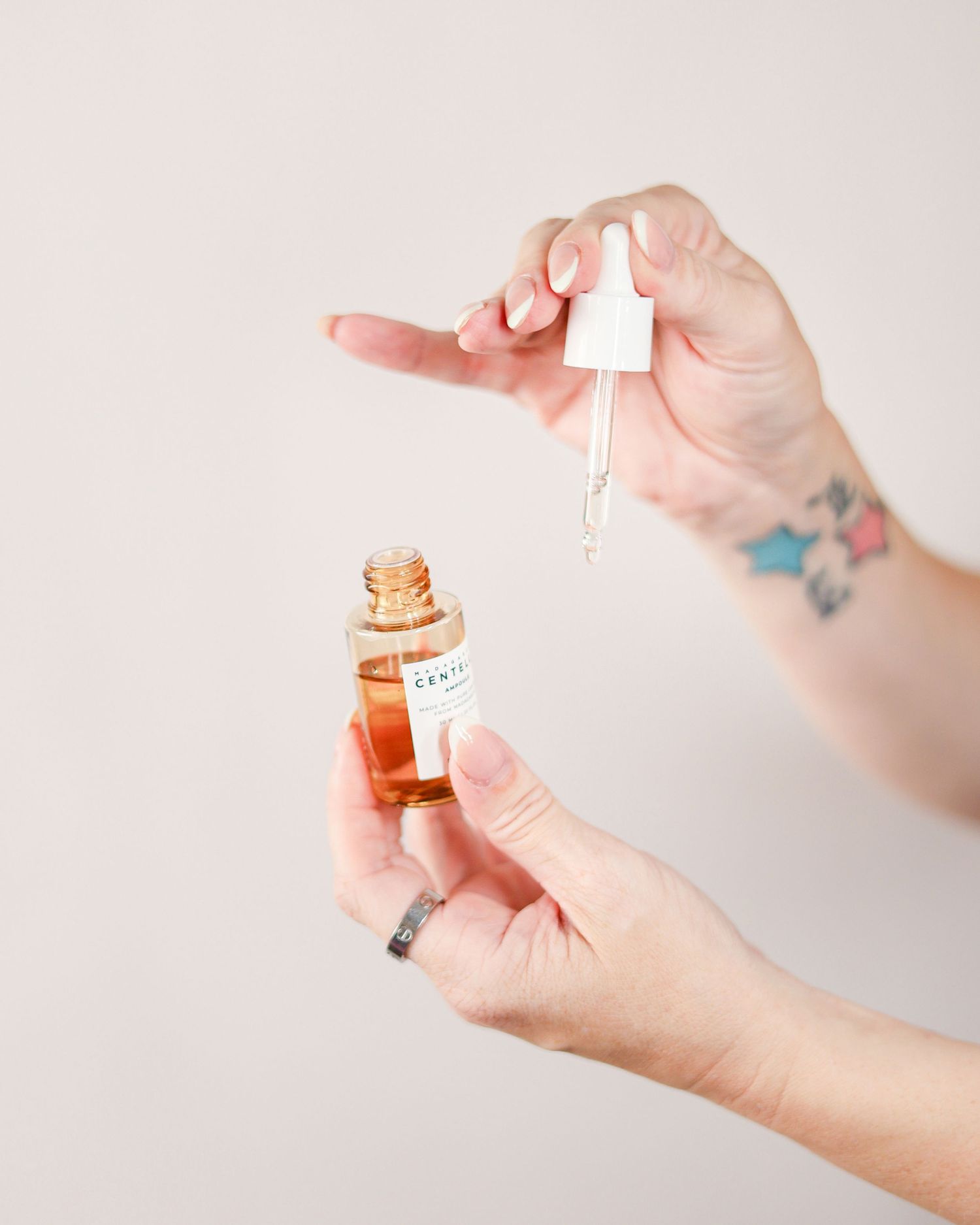 Hands with floral tattoo holding dropper bottle of facial serum, skincare product. Selsdon South London