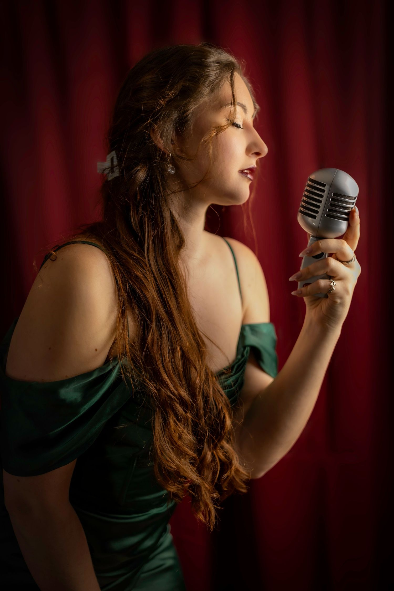 Woman in green satin dress singing into vintage microphone on stage. London