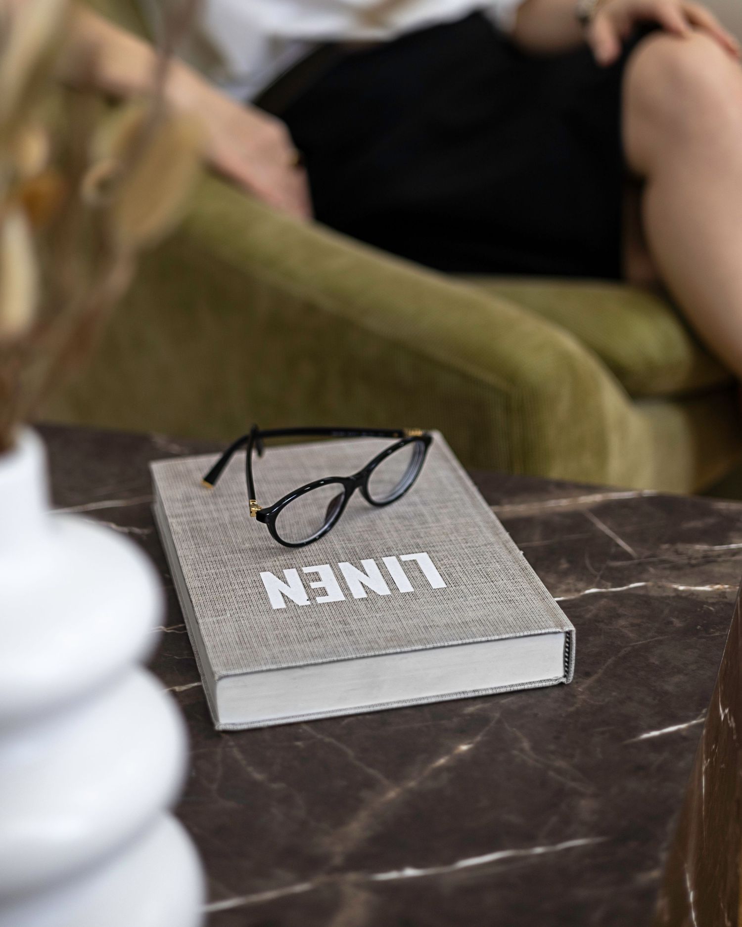 Close-up of black glasses on a gray linen book on a dark marble coffee table. Brand Photography South London