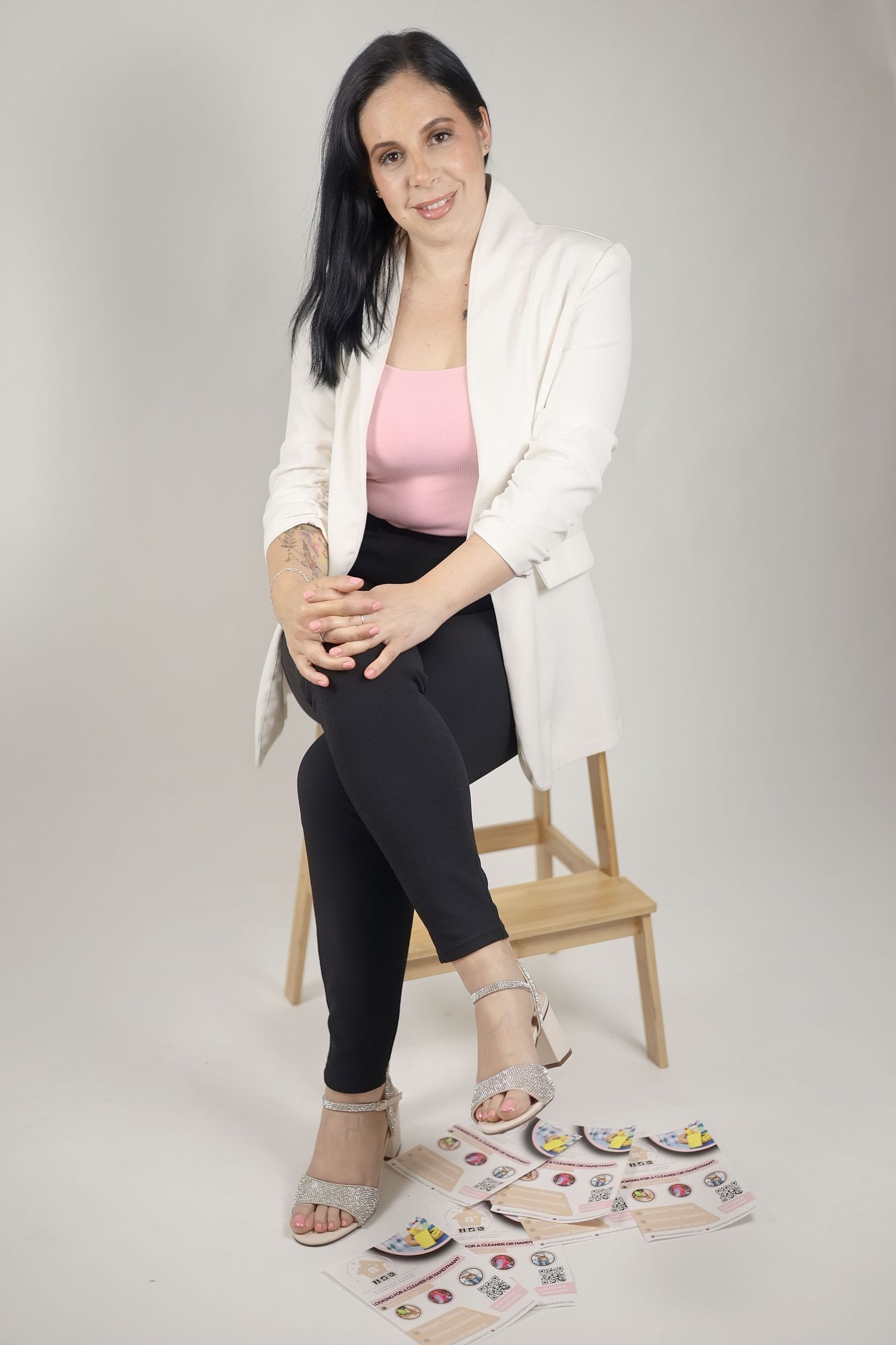 Woman in white blazer, pink top, and black leggings sitting on wooden chair with scattered cards on floor. Property service Croydon