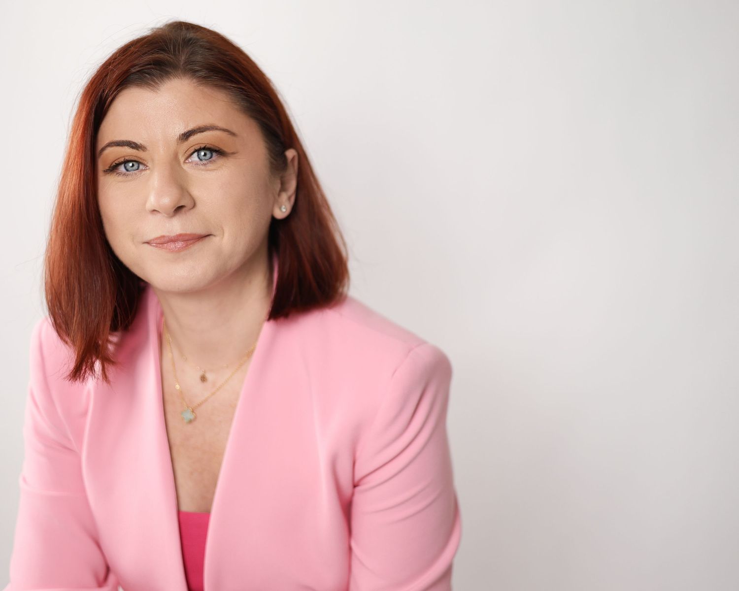 Woman with red hair in pink blazer smiling confidently against white background professional headshot. London