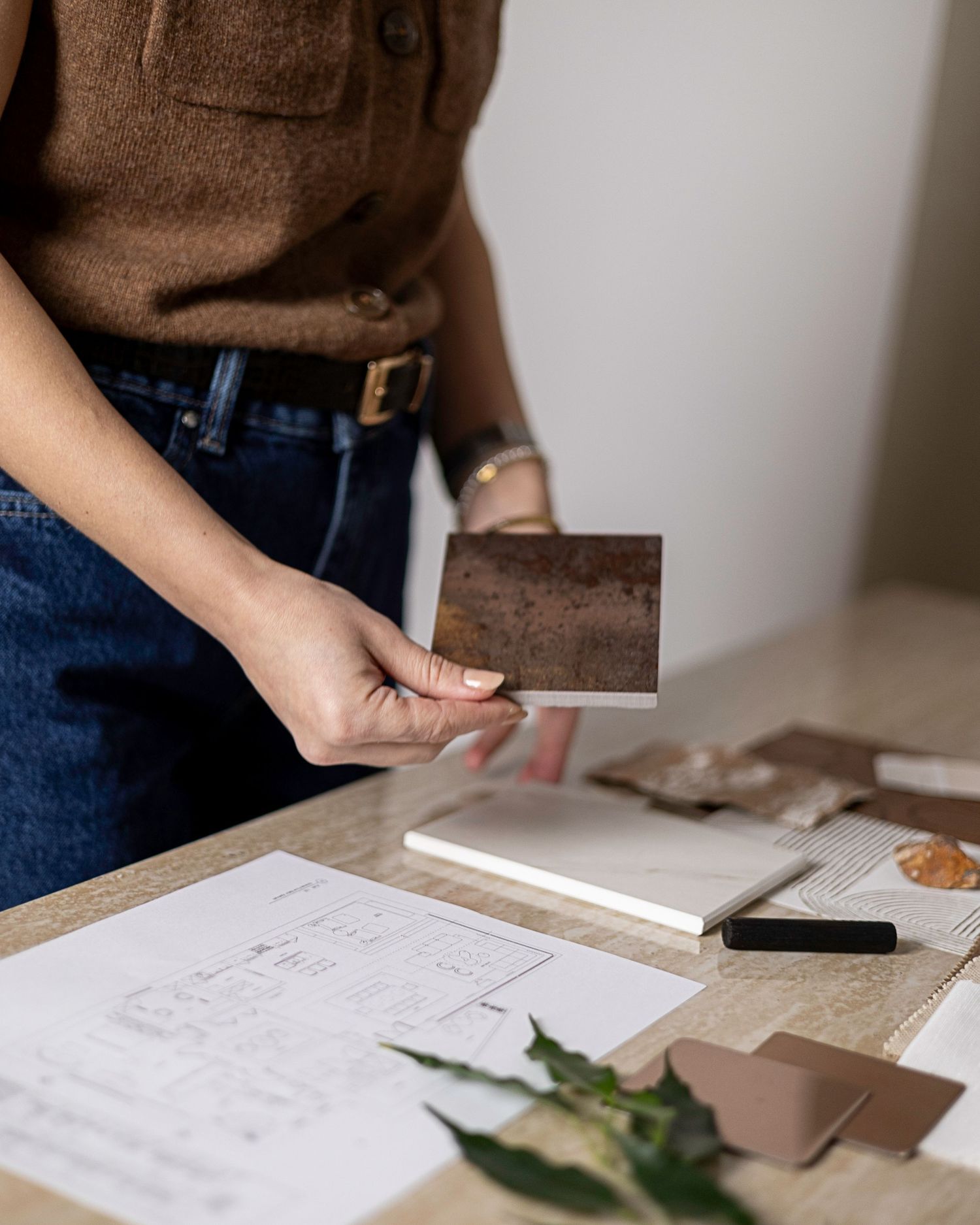 Woman in brown top holding a dark stone tile sample over an interior design workspace. Brand Photography South London