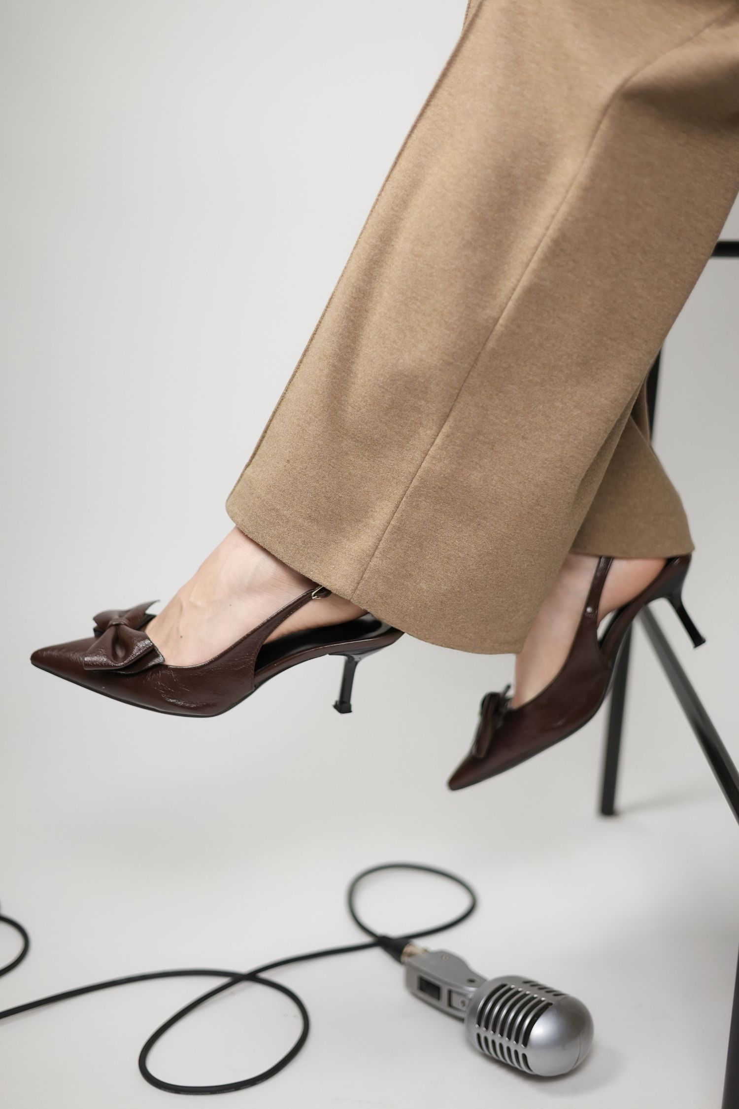 Close-up of womens legs in beige trousers and brown bow heels with a vintage microphone on the floor. Brand Photography South London