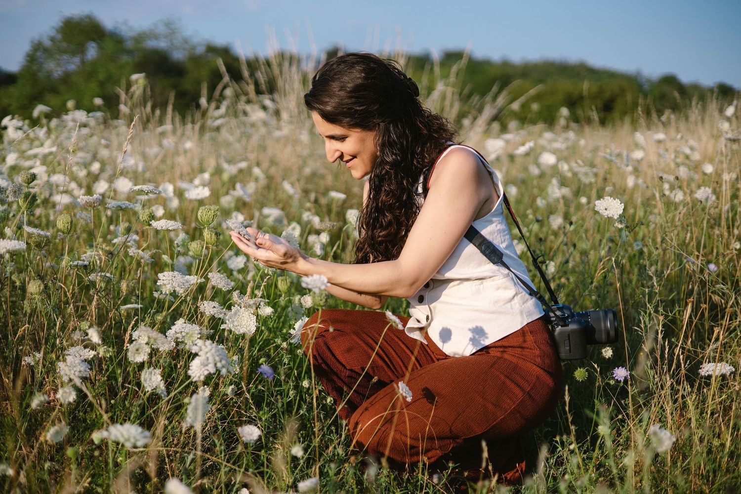 Woman crouching in a wildflower meadow, photographing white flowers on a sunny day. Brand Photography South London