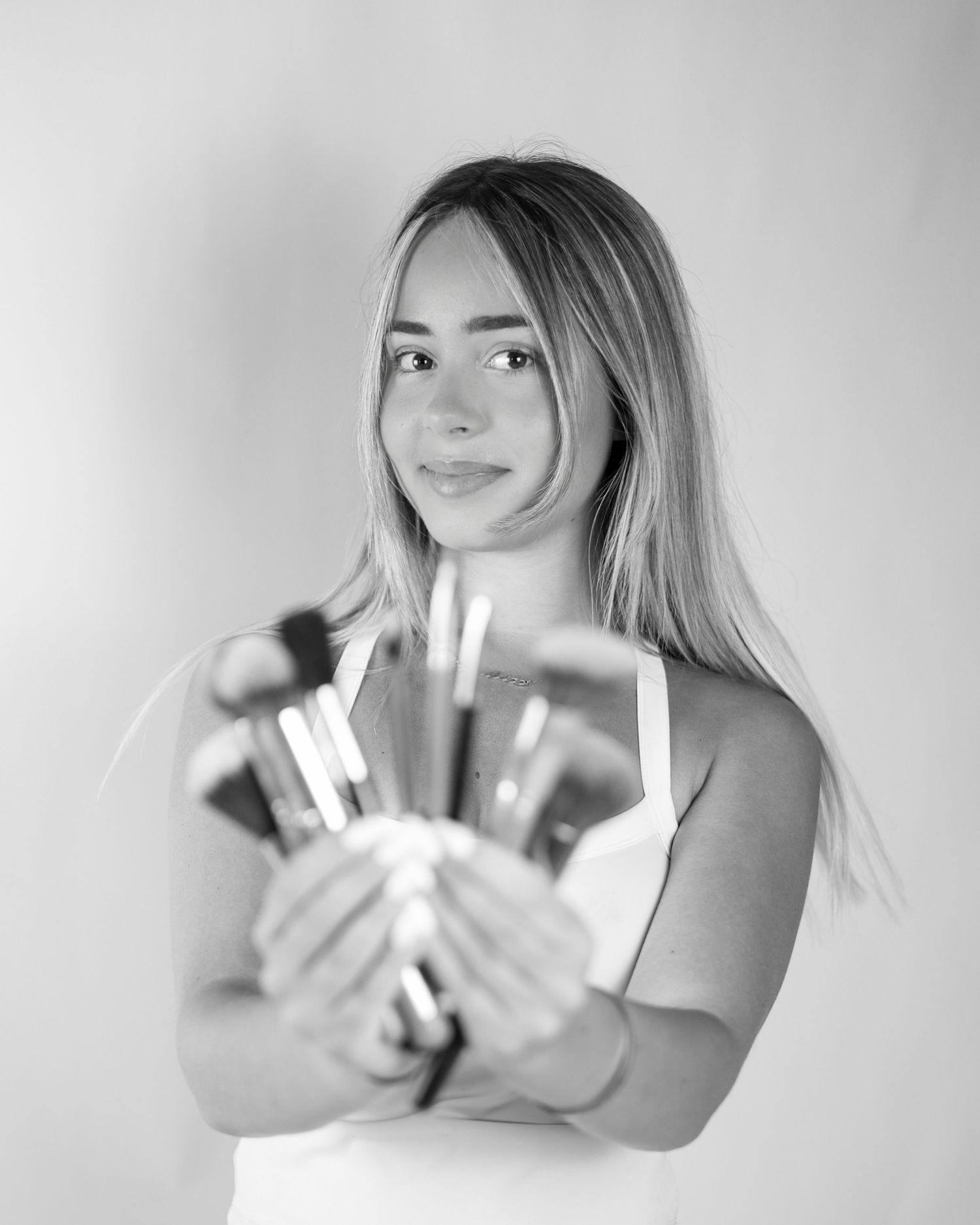 Black and white portrait of young blonde woman holding makeup brushes, beauty professional. South London