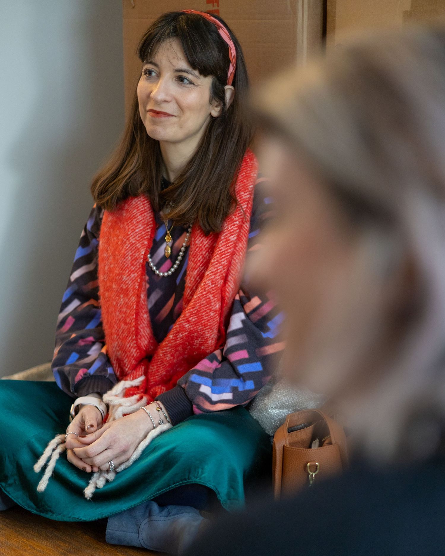Brunette woman in colorful patterned top with red scarf sitting cross-legged in a mindful setting. Copywriter in London