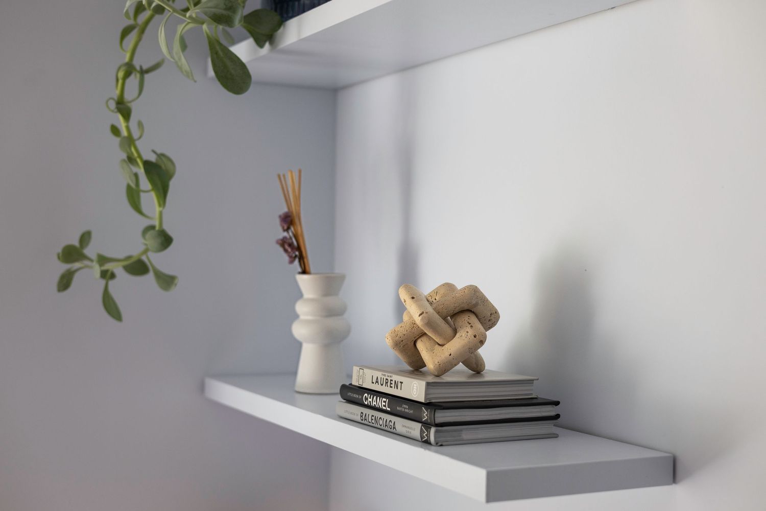 Minimalist shelf decor with a white vase, reed diffuser, stacked books, and a wooden knot sculpture. Brand Photography South London