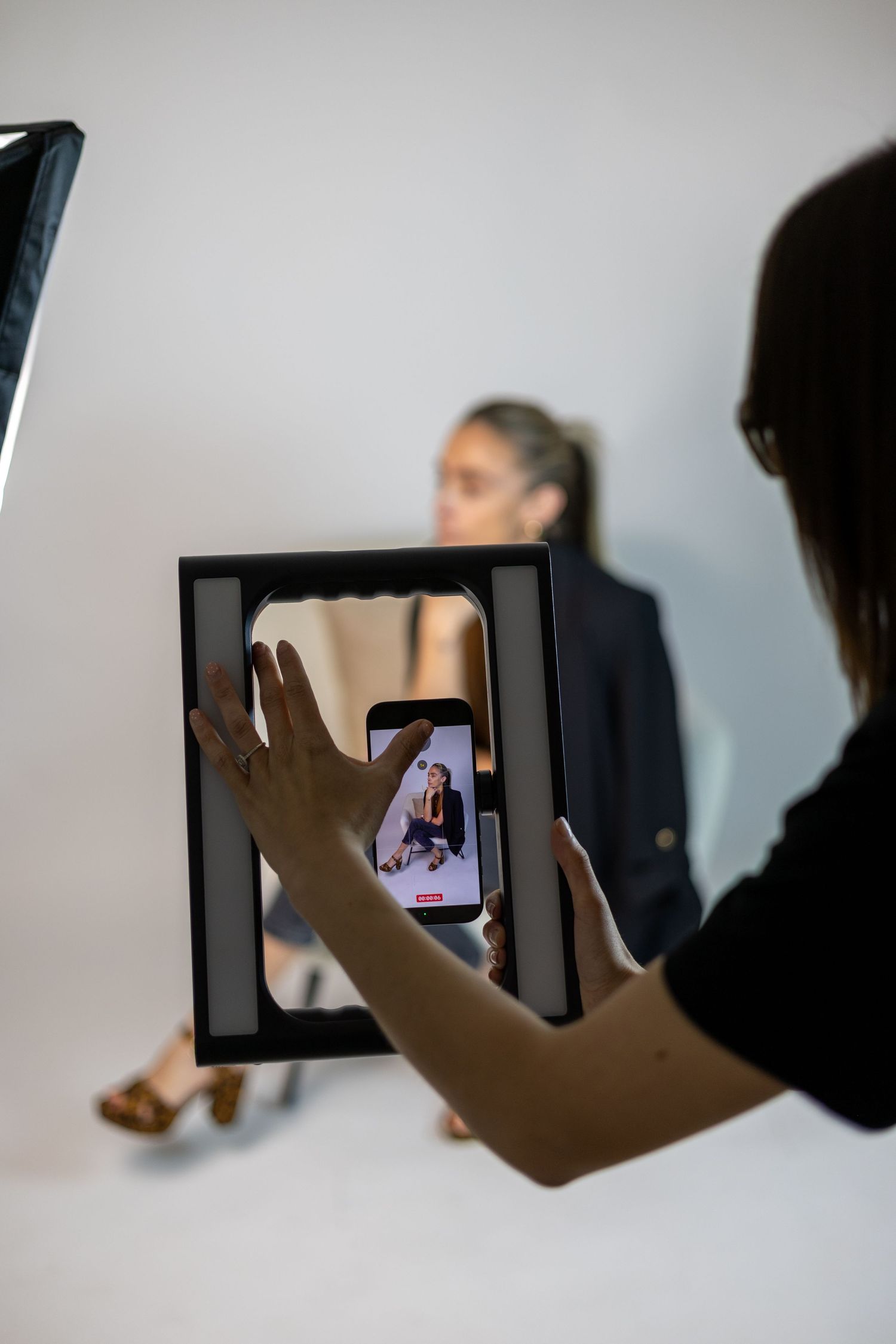 Photographer holding smartphone to capture model during studio photoshoot.