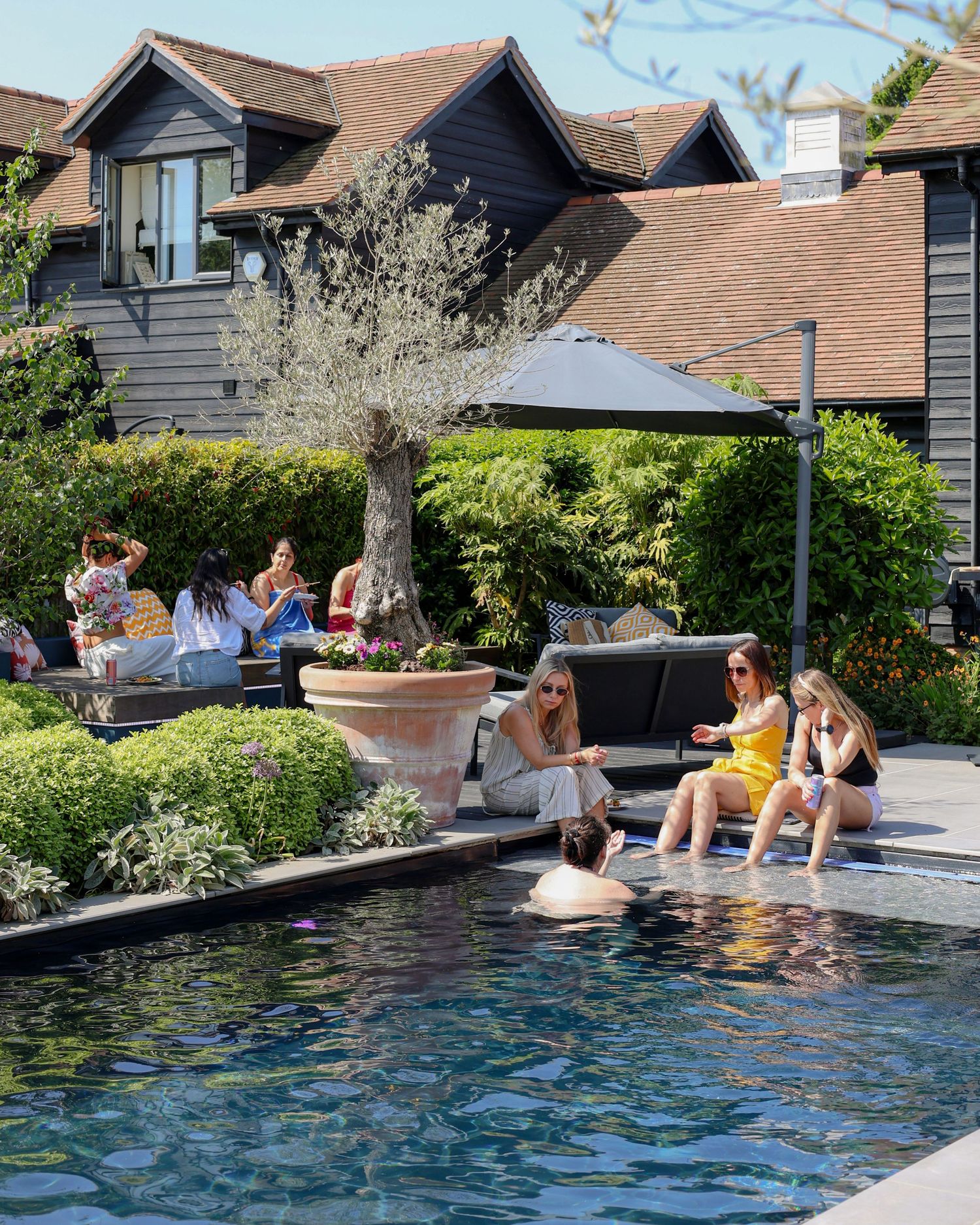 Women relaxing poolside at a luxury hotel garden spa on a sunny day. Brand Photography South London