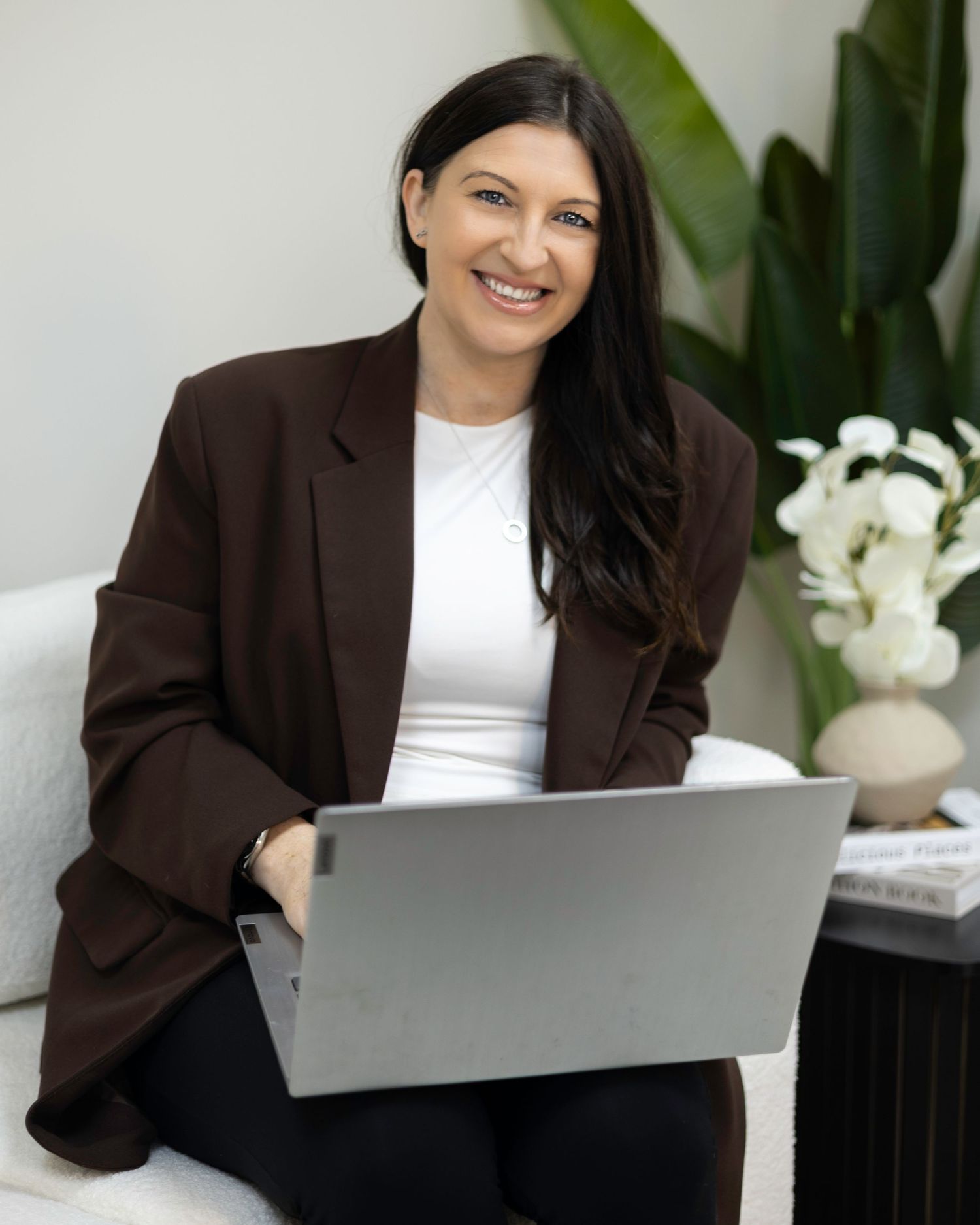 Smiling woman in brown blazer working on laptop in modern interior. South London