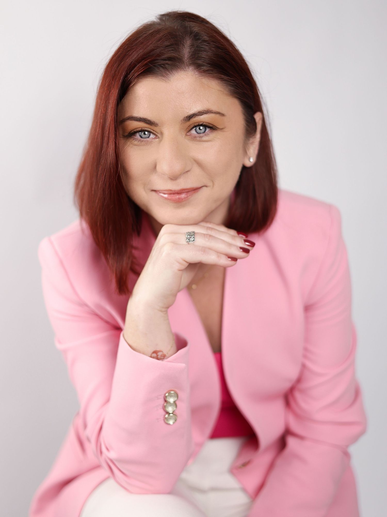 Professional woman in pink blazer with red hair and blue eyes posing confidently for a business portrait photo. London