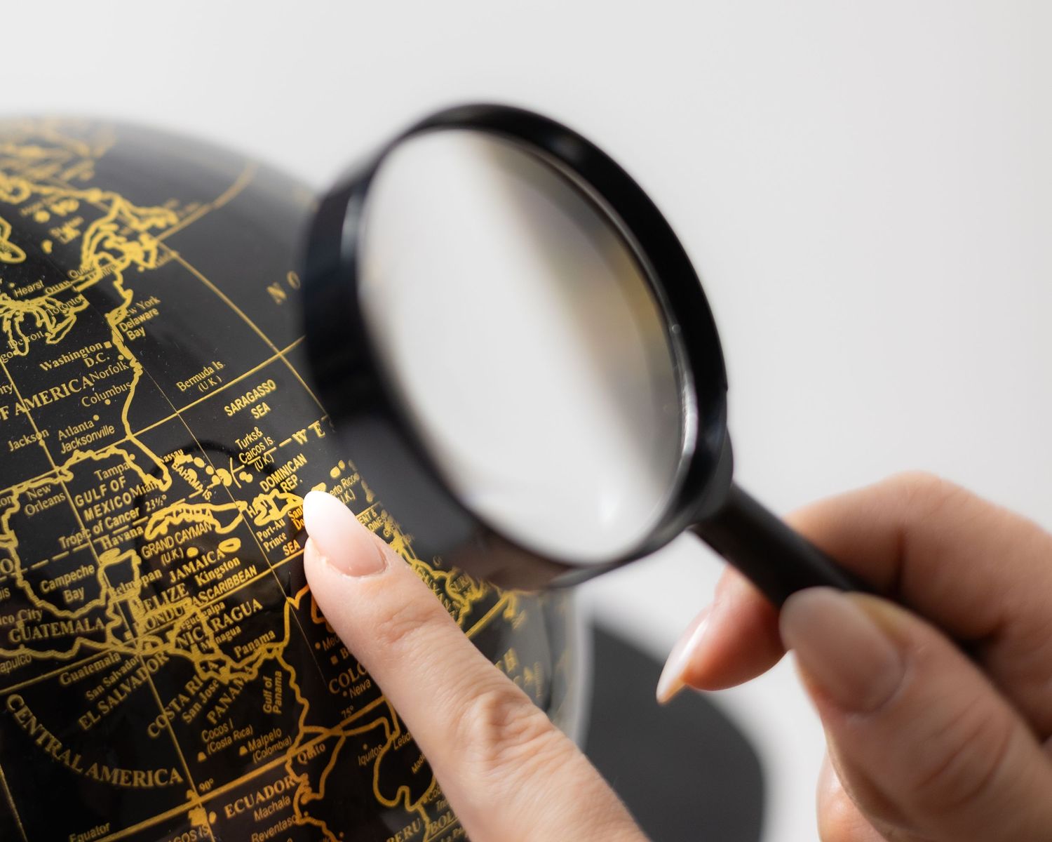 Hand holding magnifying glass over dark globe showing gold world map details. South London