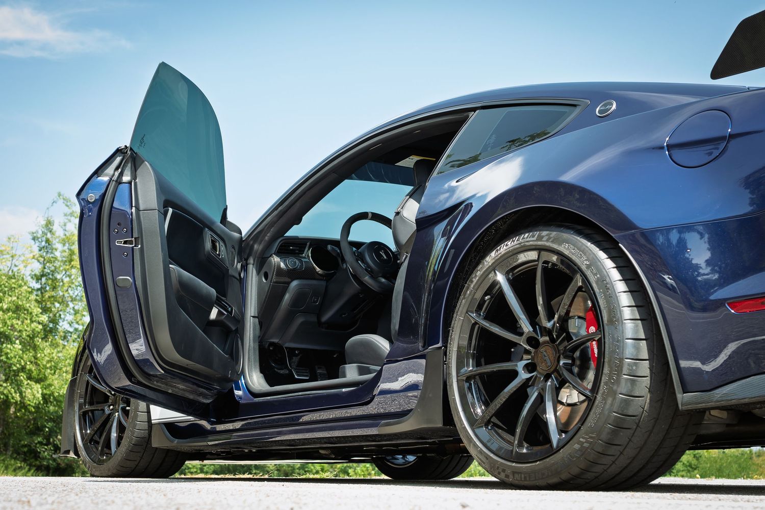 Dark blue Ford Mustang Shelby GT500 with lambo-style doors open, showcasing black alloy wheels with red brake calipers.