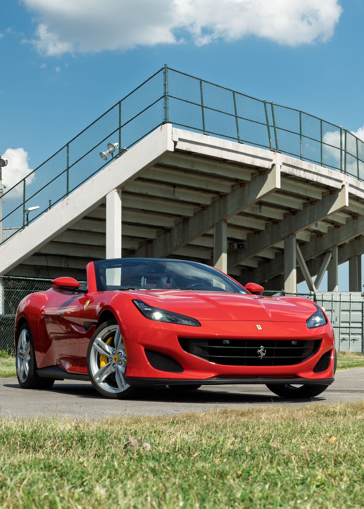 Red Ferrari Portofino convertible with top down parked near a concrete grandstand on a sunny day.