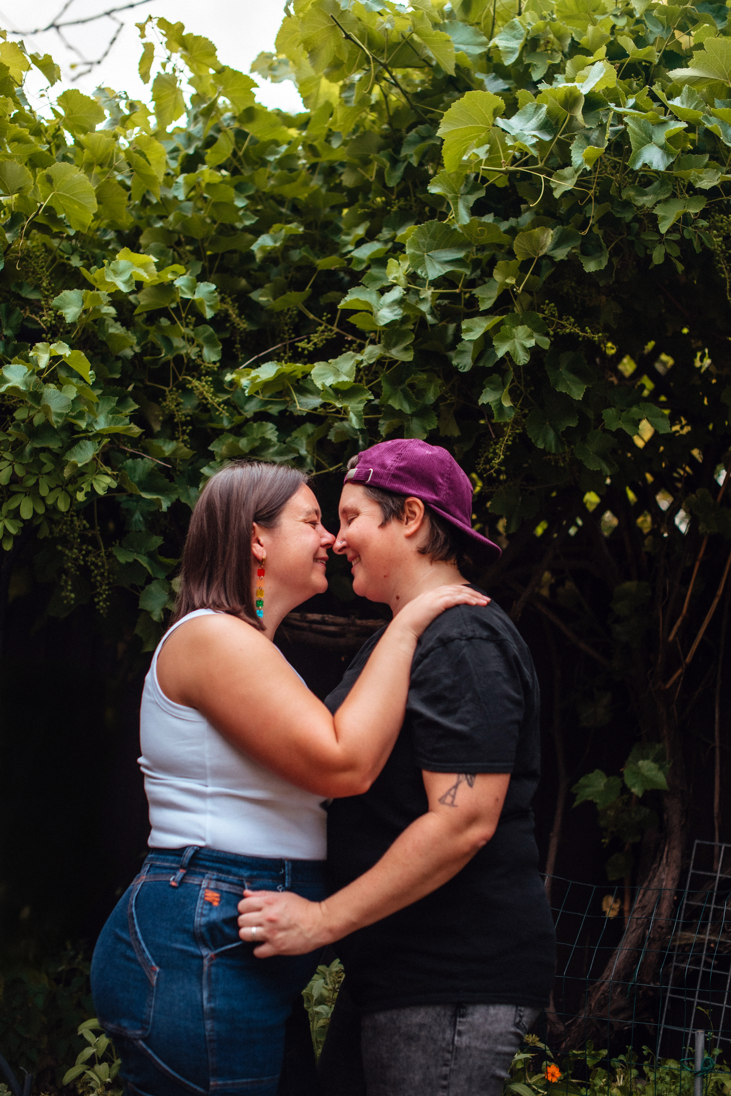 Two people sharing a romantic moment outdoors, surrounded by lush green vines in a garden setting.