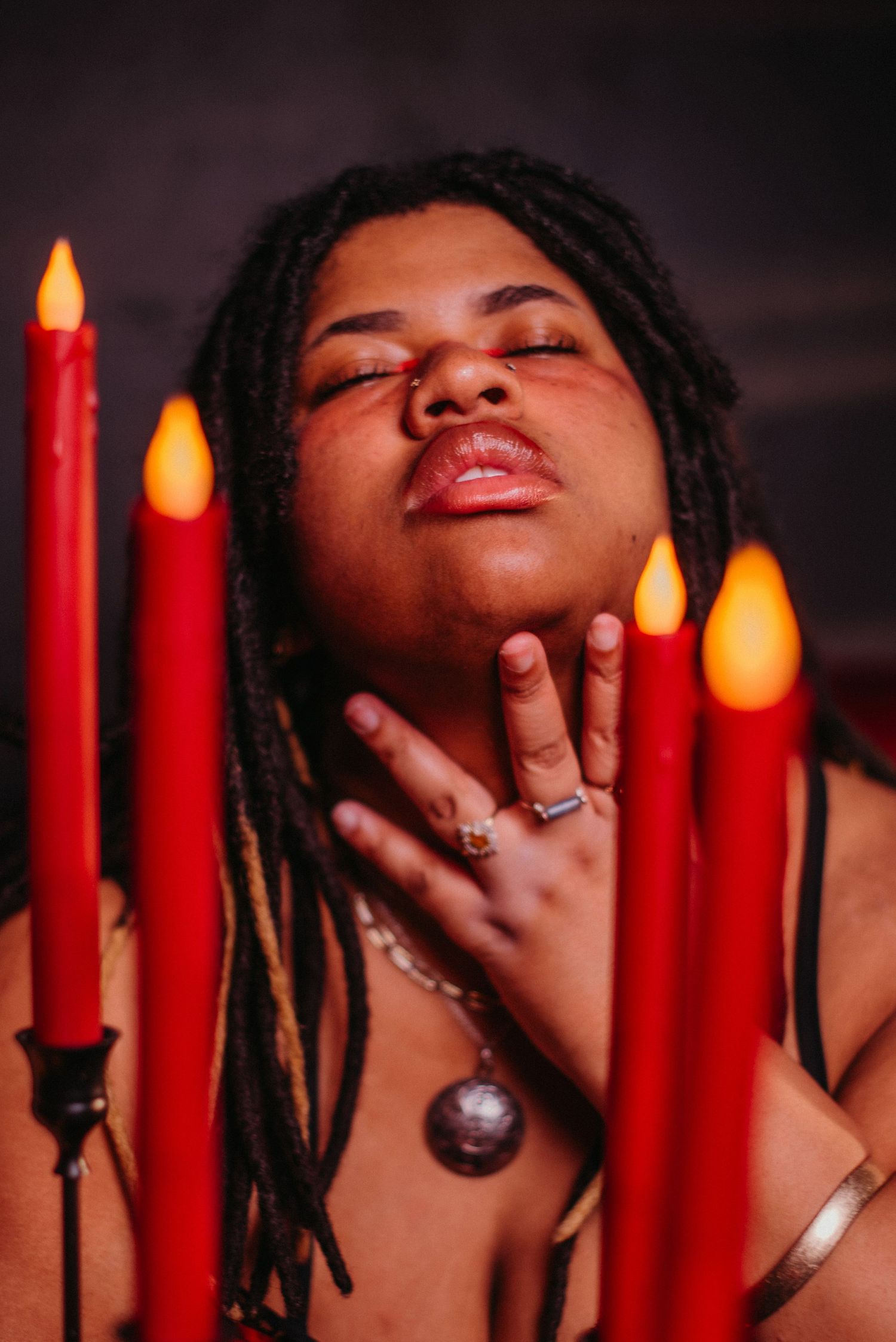 Person with dreadlocks posing with red candles in moody candlelit portrait photography.