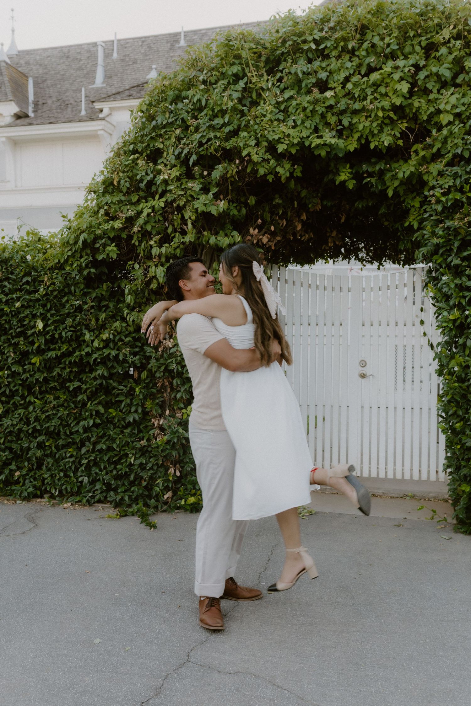 Romantic couple hugging and laughing near a ivy-covered white garden gate.