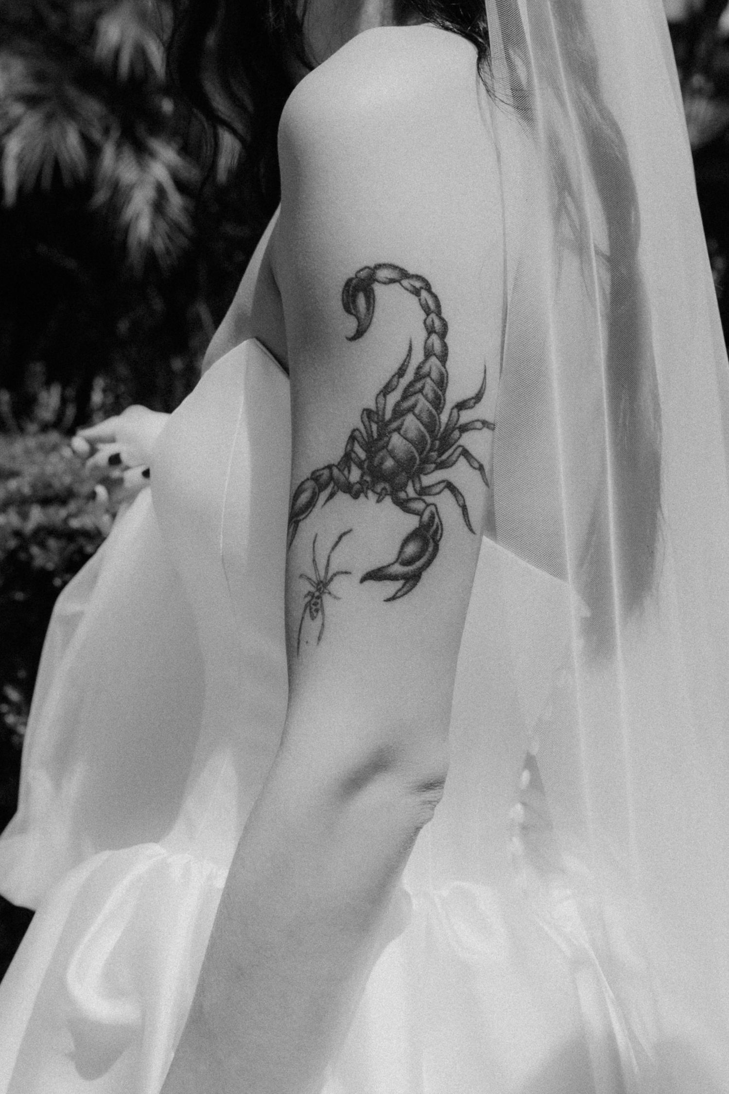 Black and white photo of a bride's upper arm featuring a detailed scorpion tattoo with a small spider.