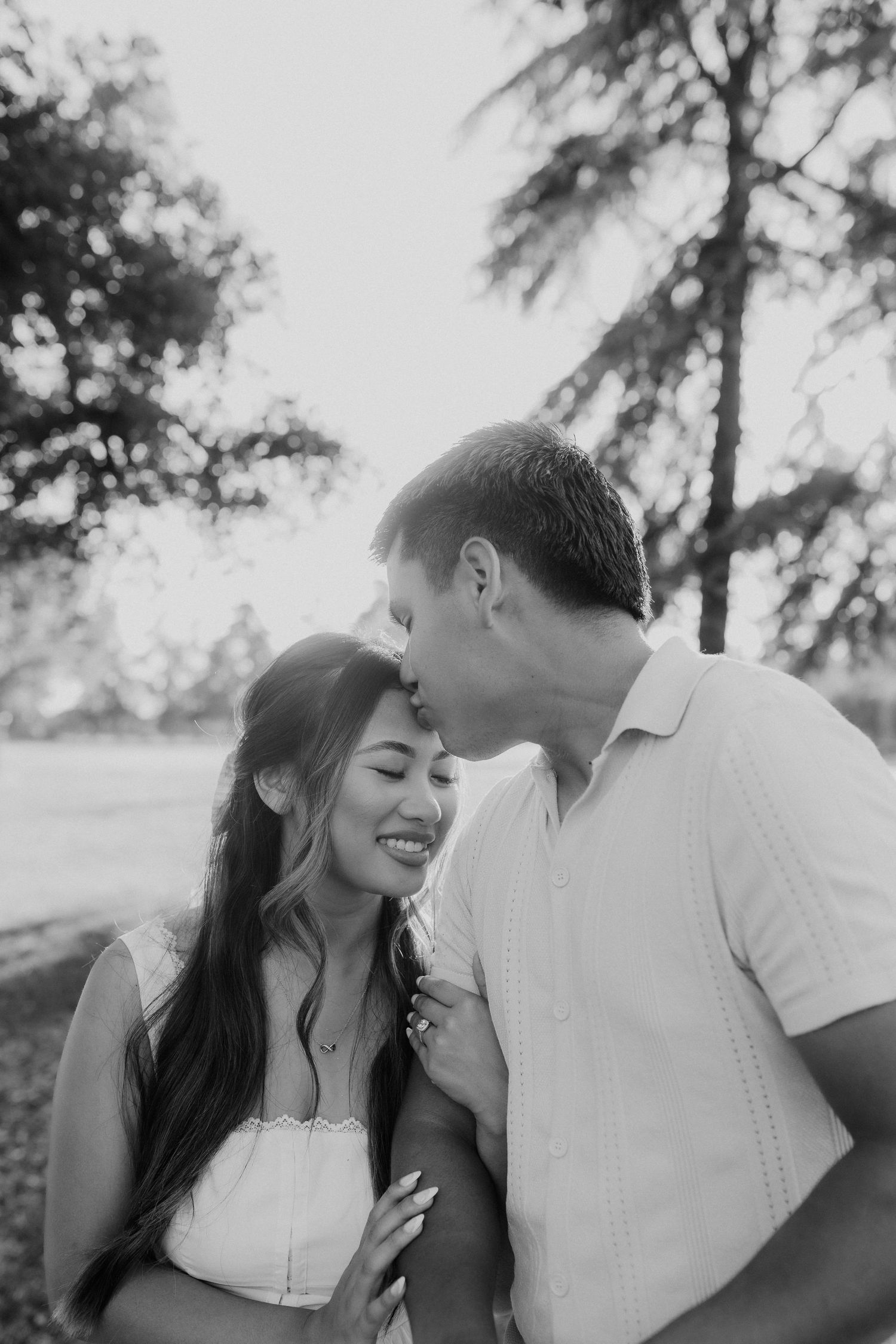 Black and white photo of a couple sharing a tender moment outdoors, man kissing woman on forehead.
