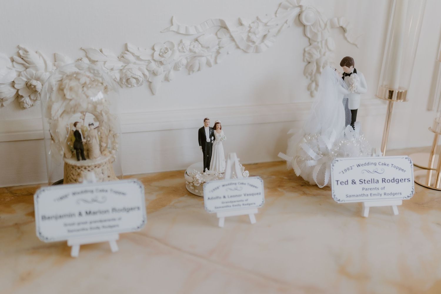 Three vintage wedding cake toppers displayed with personalized name signs on elegant marble surface.