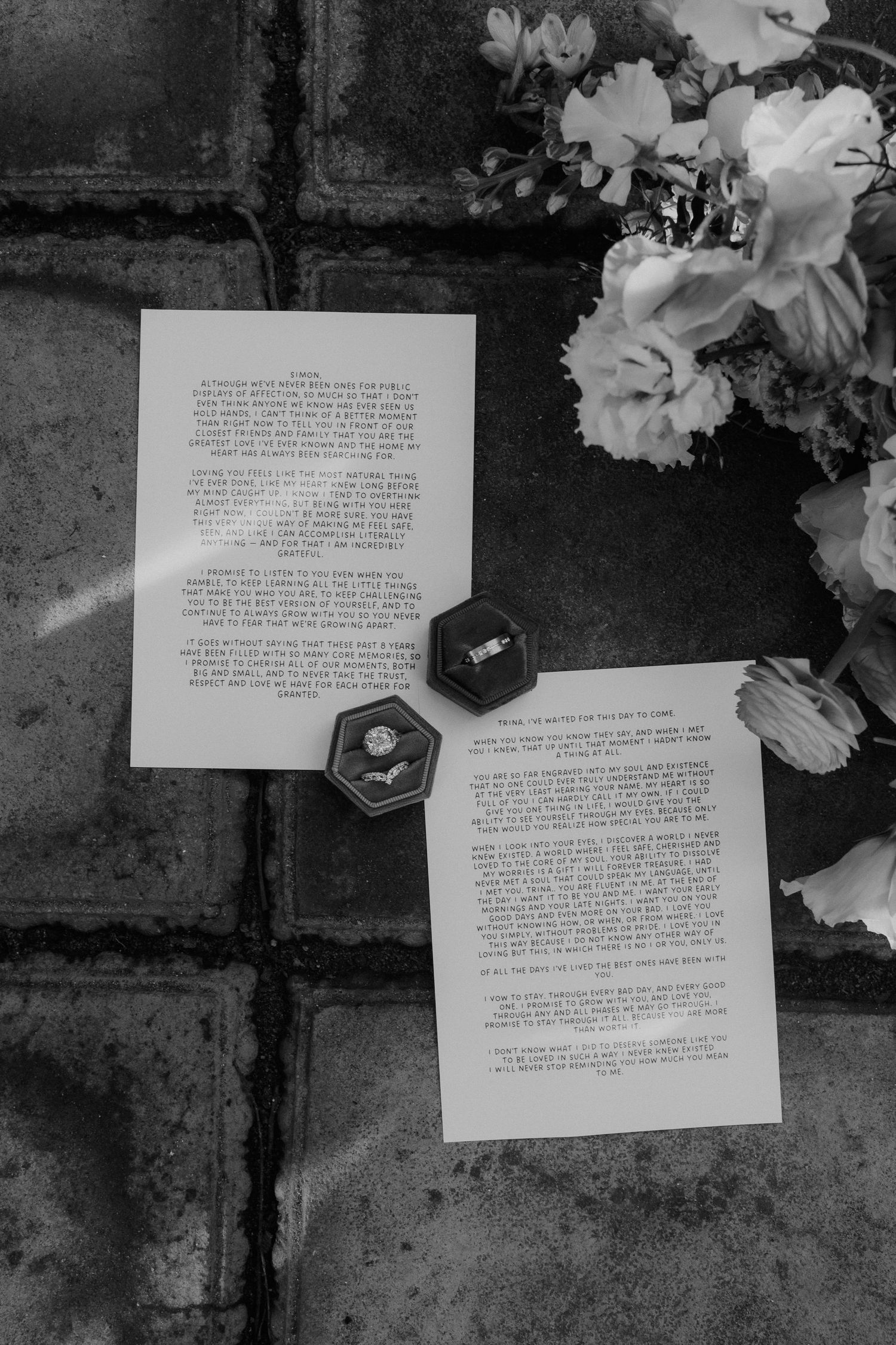 Black and white flat lay of wedding vows, diamond ring in hexagon box, and floral bouquet.