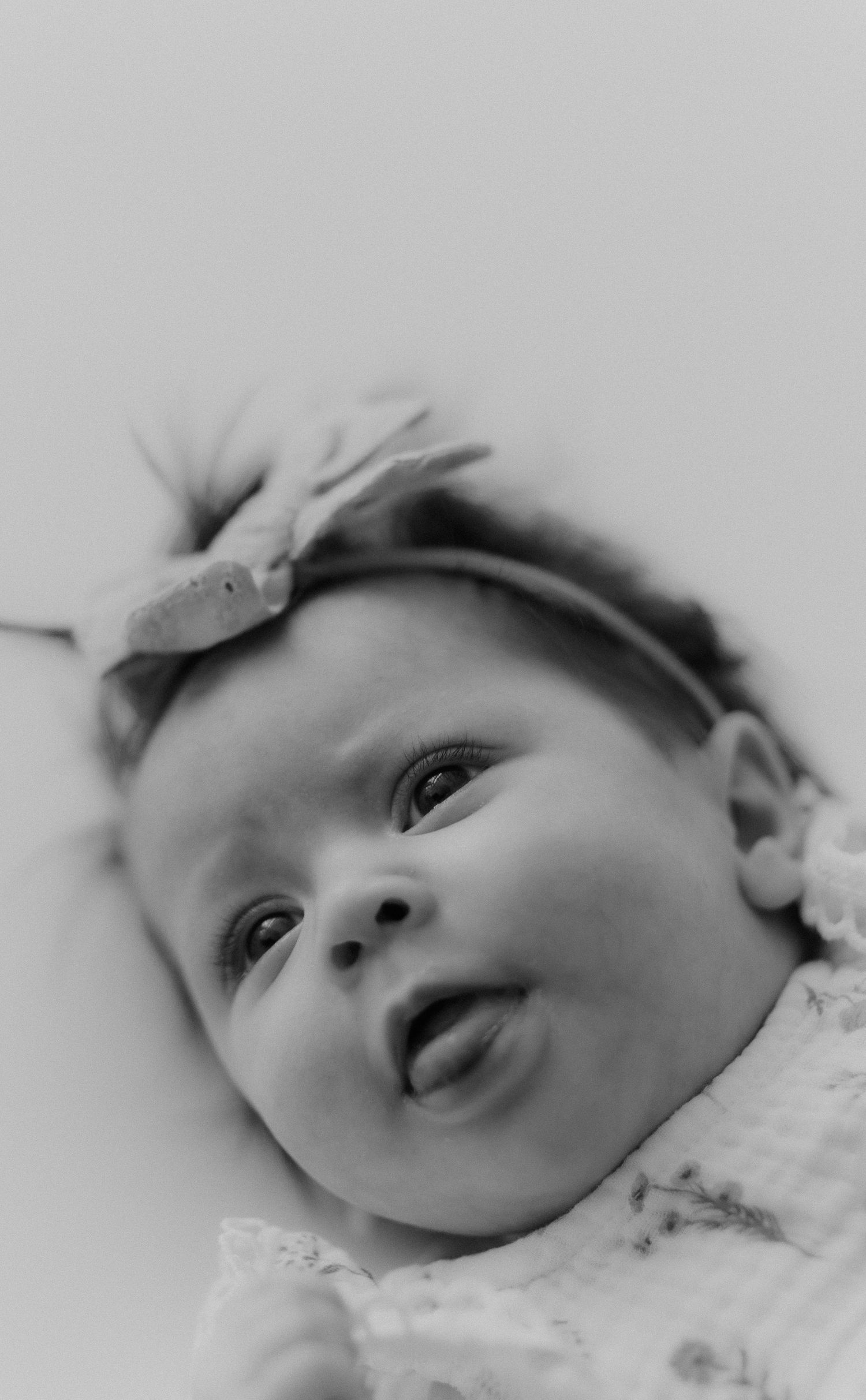 Black and white portrait of newborn baby girl with bow headband sticking tongue out.