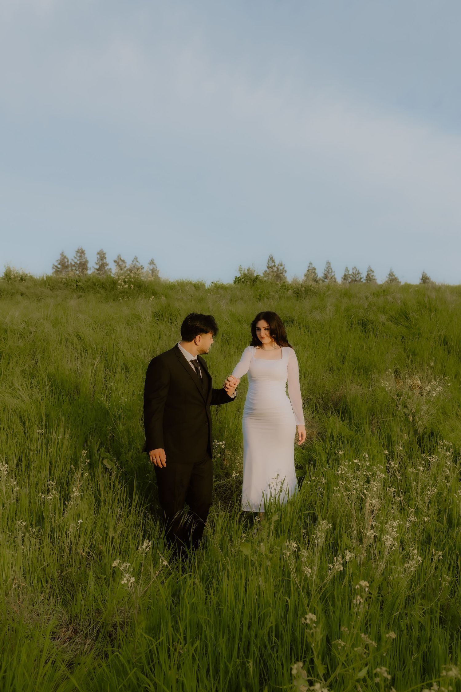 Couple holding hands walking through a wildflower meadow in formal wedding attire. Fresno California