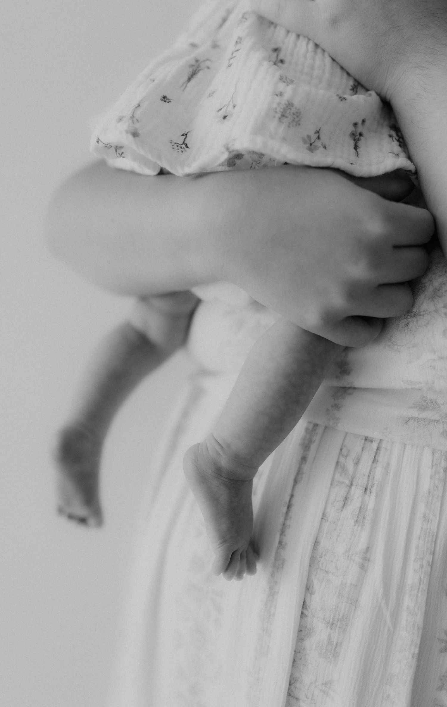 Black and white close-up of a mother in a white dress gently holding a baby, focusing on the infant tiny feet.