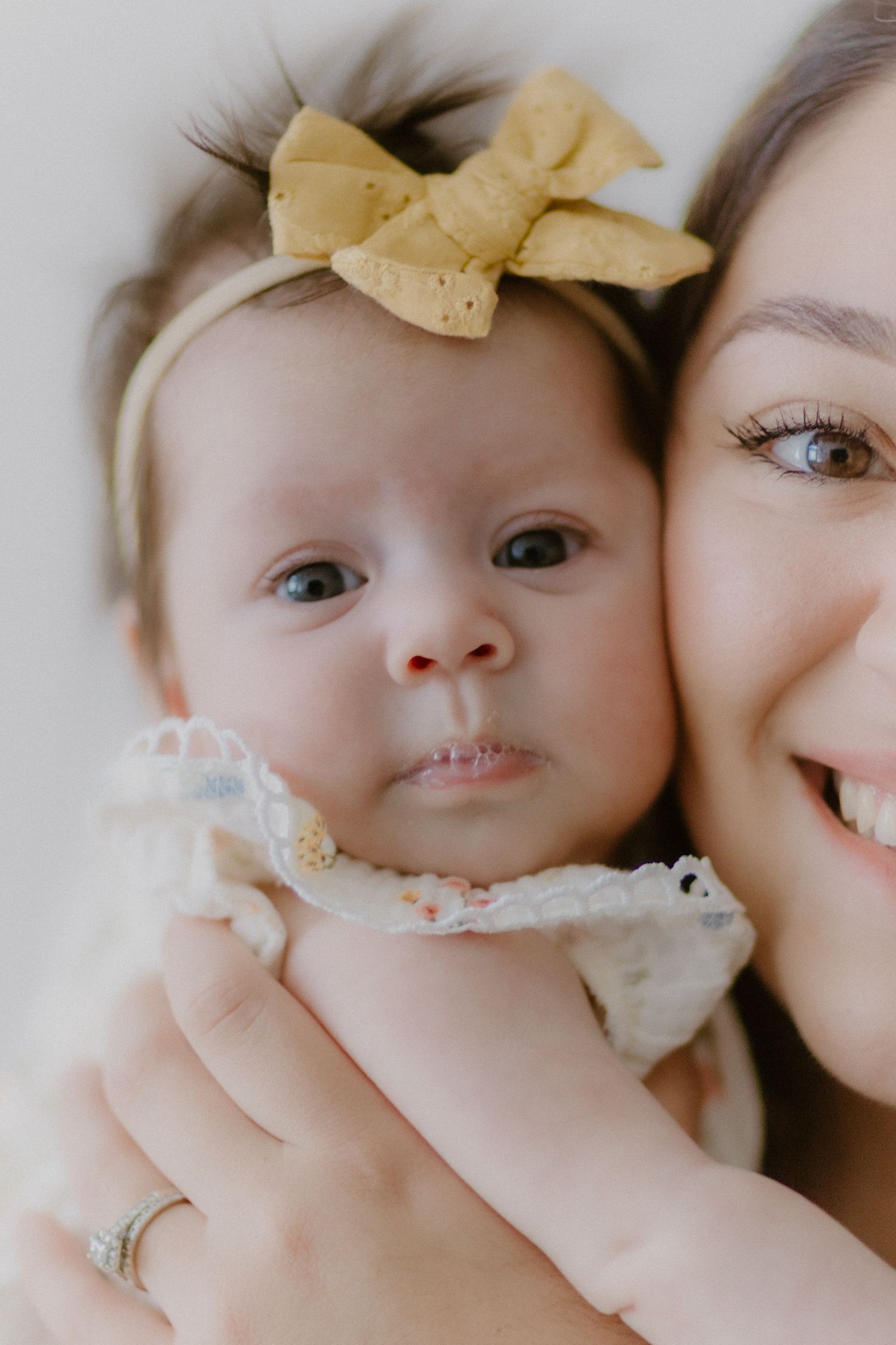 Close-up of smiling mother holding newborn baby girl wearing a yellow bow headband.