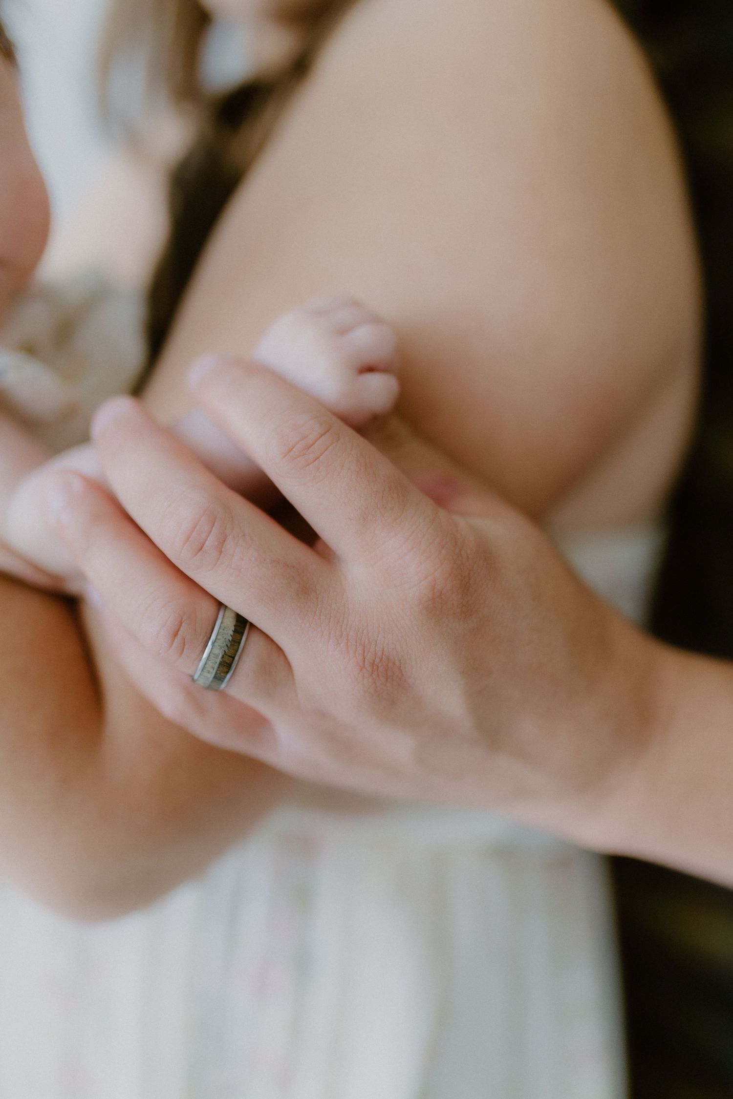 Close-up of a fathers hand wearing a wedding band tenderly holding his newborn babys tiny foot.