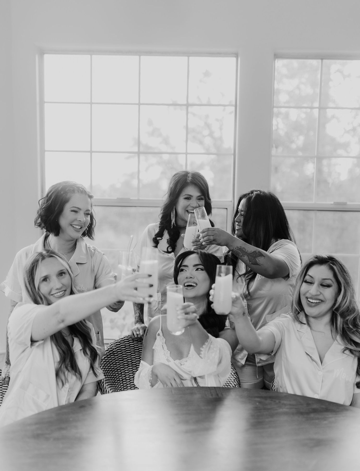 Black and white photo of bride and bridesmaids in robes toasting with drinks before the wedding ceremony.