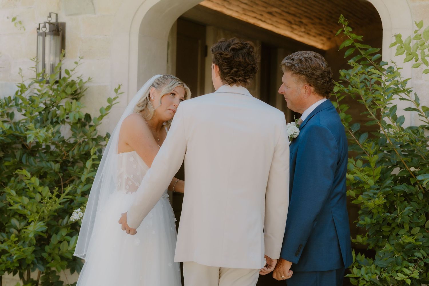 Bride and groom holding hands with wedding officiant during an outdoor ceremony at a stone venue.