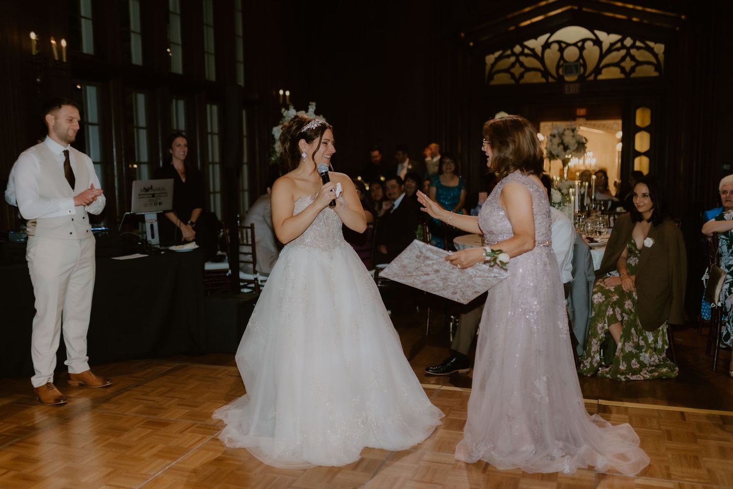Bride laughs joyfully while dancing with guest in elegant wood-paneled ballroom during wedding reception.