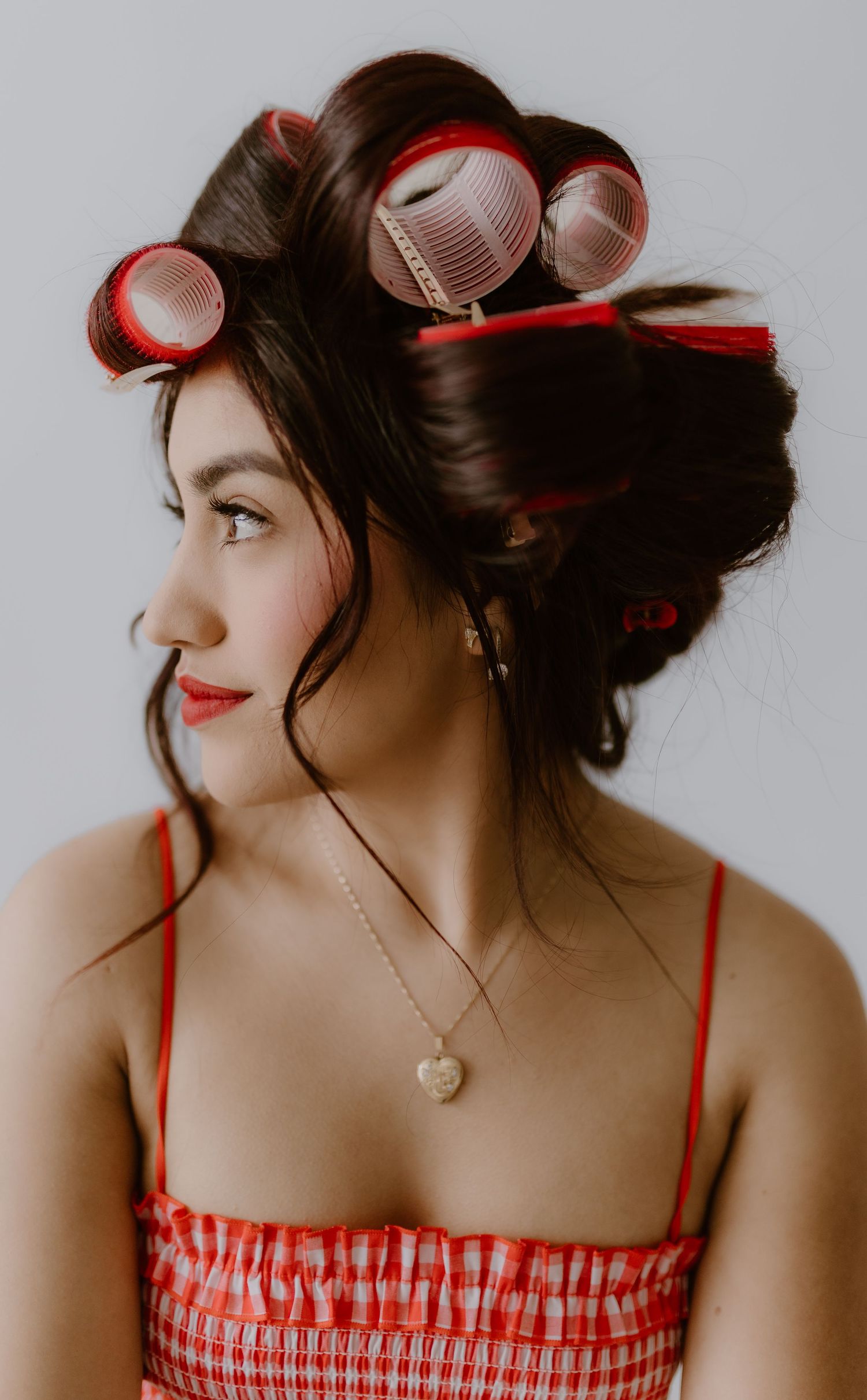 Close-up profile of brunette woman with red hair rollers wearing red gingham dress and heart necklace. Branding Tulare, California
