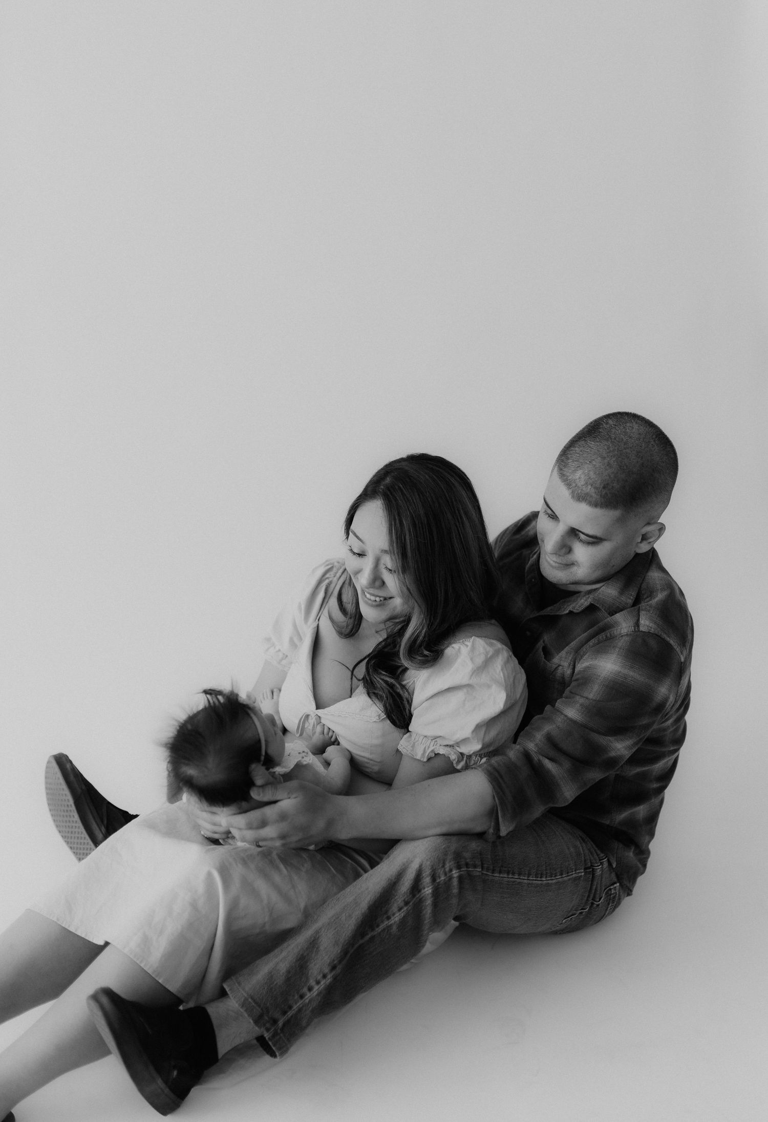 Black and white photo of a young couple sitting on the floor lovingly holding their newborn.