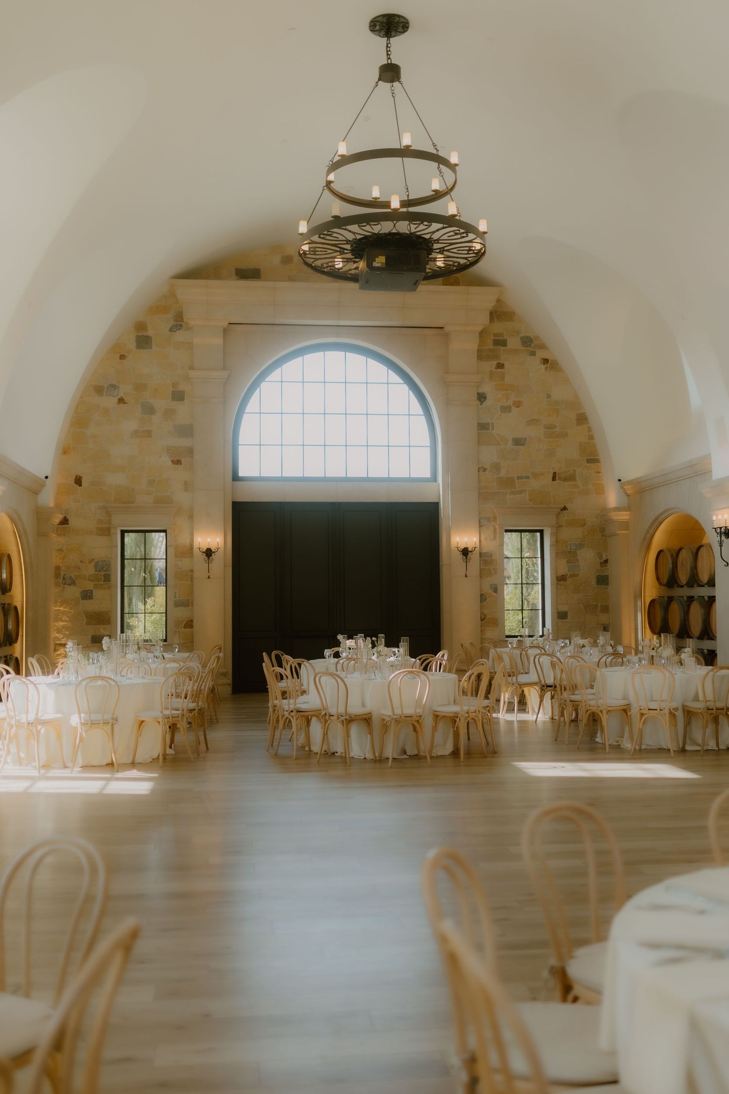 Stunning barrel-vaulted stone wedding reception hall with chandelier, round tables, and arched window. reception fallbrook California