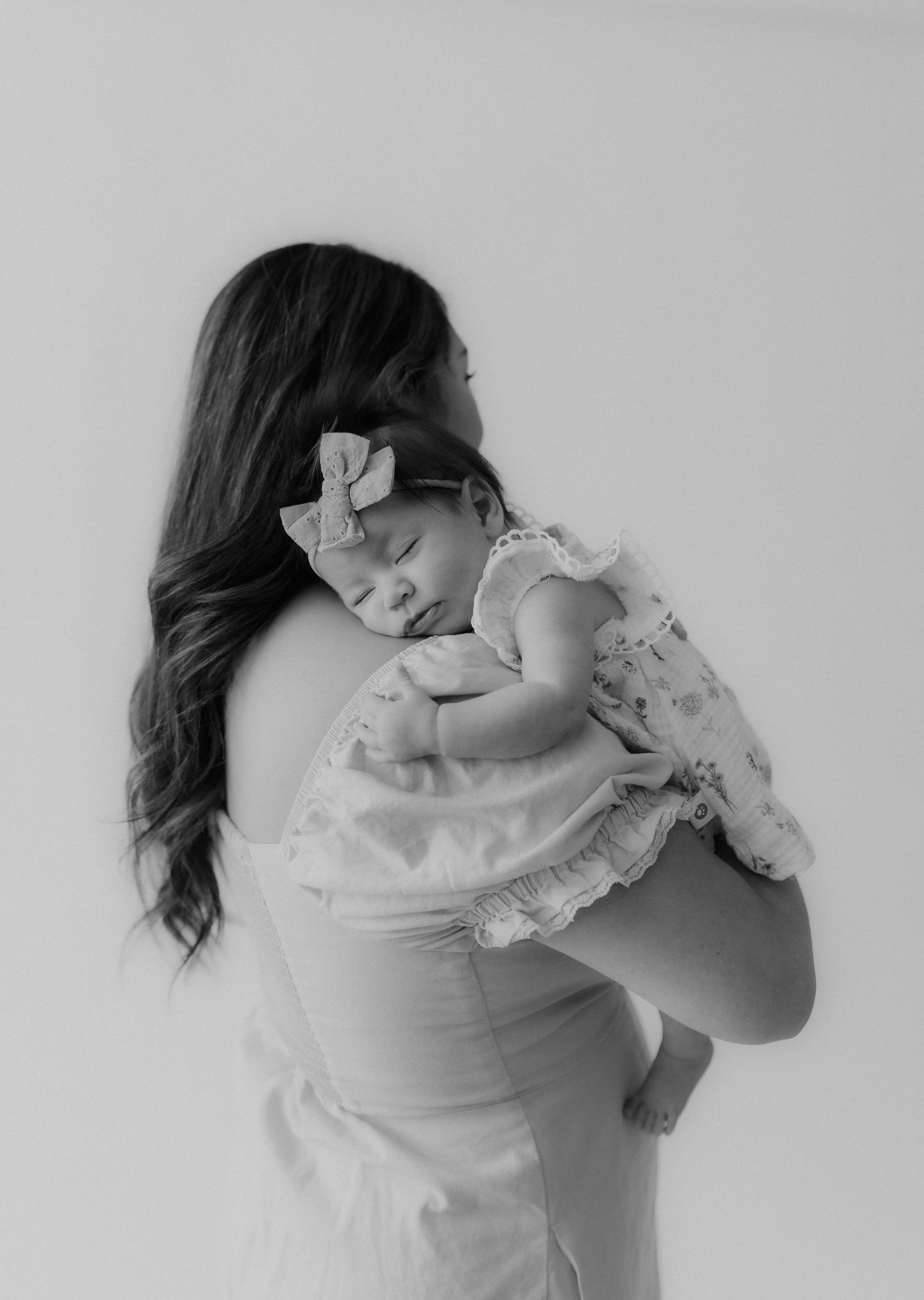 Black and white photo of mother holding sleeping newborn baby on her shoulder.