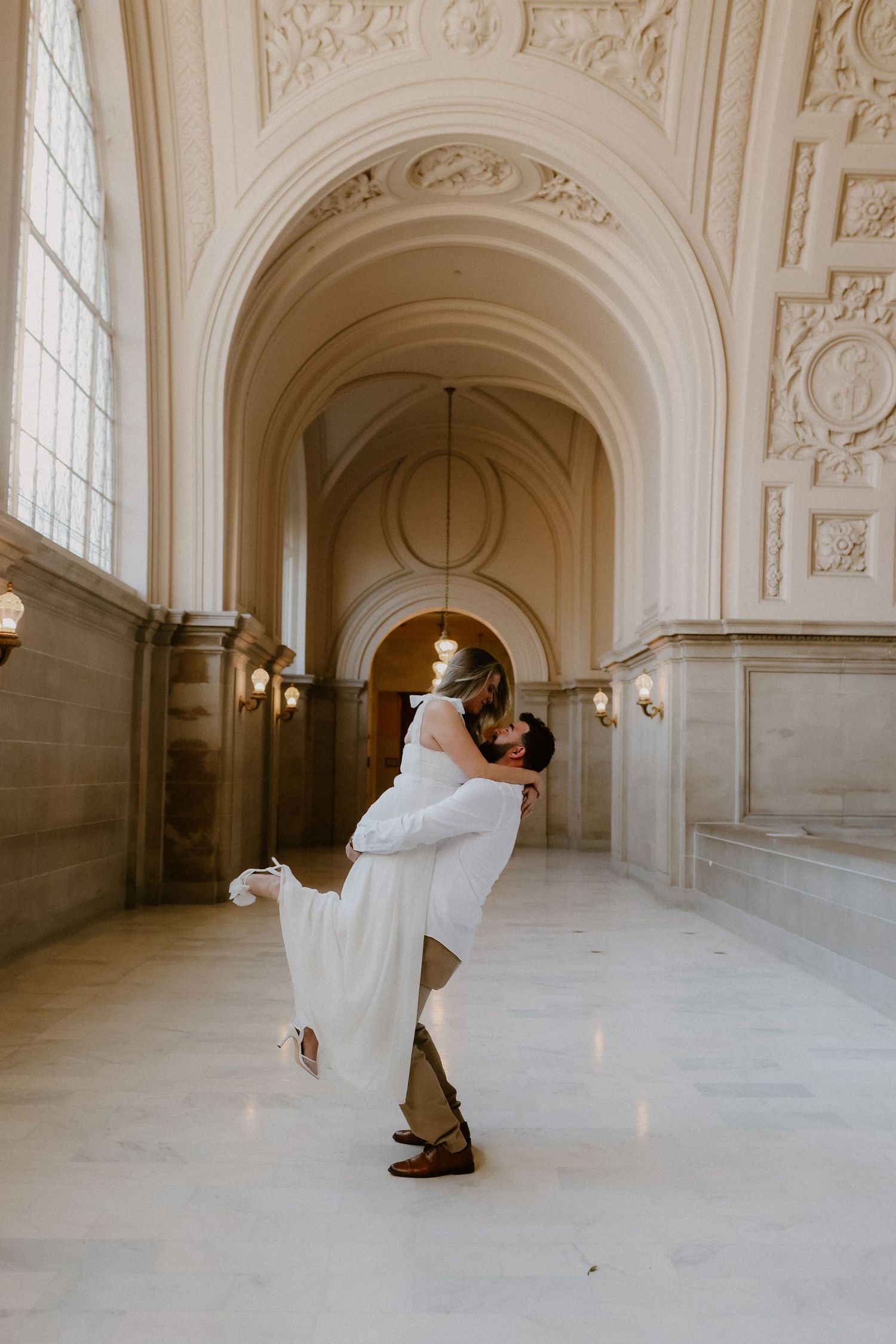 Groom lifting bride in elegant San Francisco City Hall wedding portrait.