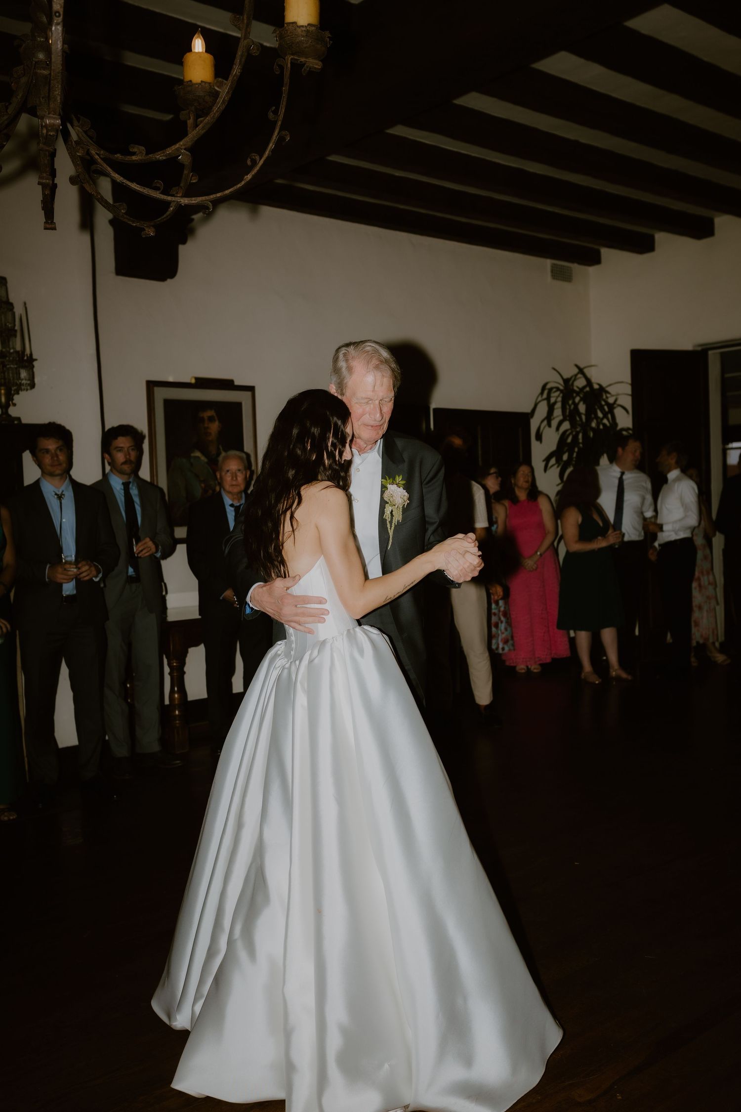 Bride in white satin ballgown dancing with older gentleman at wedding reception.