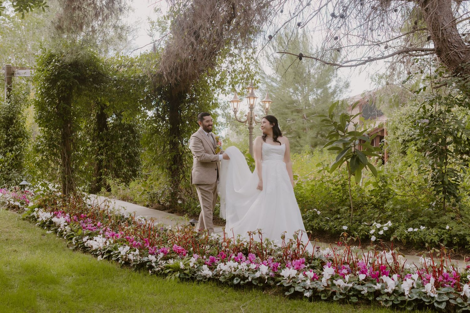 Bride and groom walking through a lush garden pathway lined with colorful flowers at their wedding.