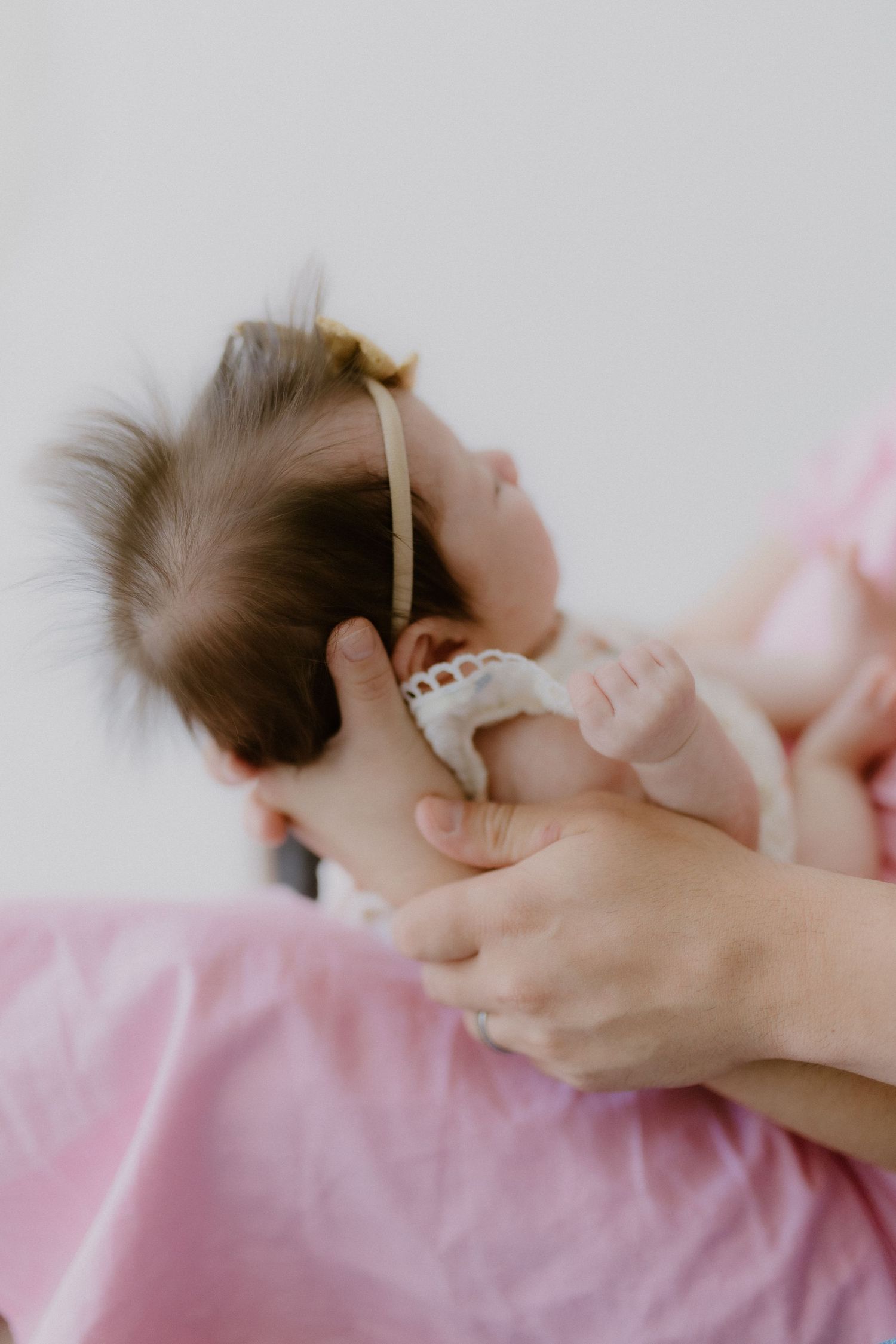 Close-up of a newborn baby with a gold bow headband being cradled in mother's hands.