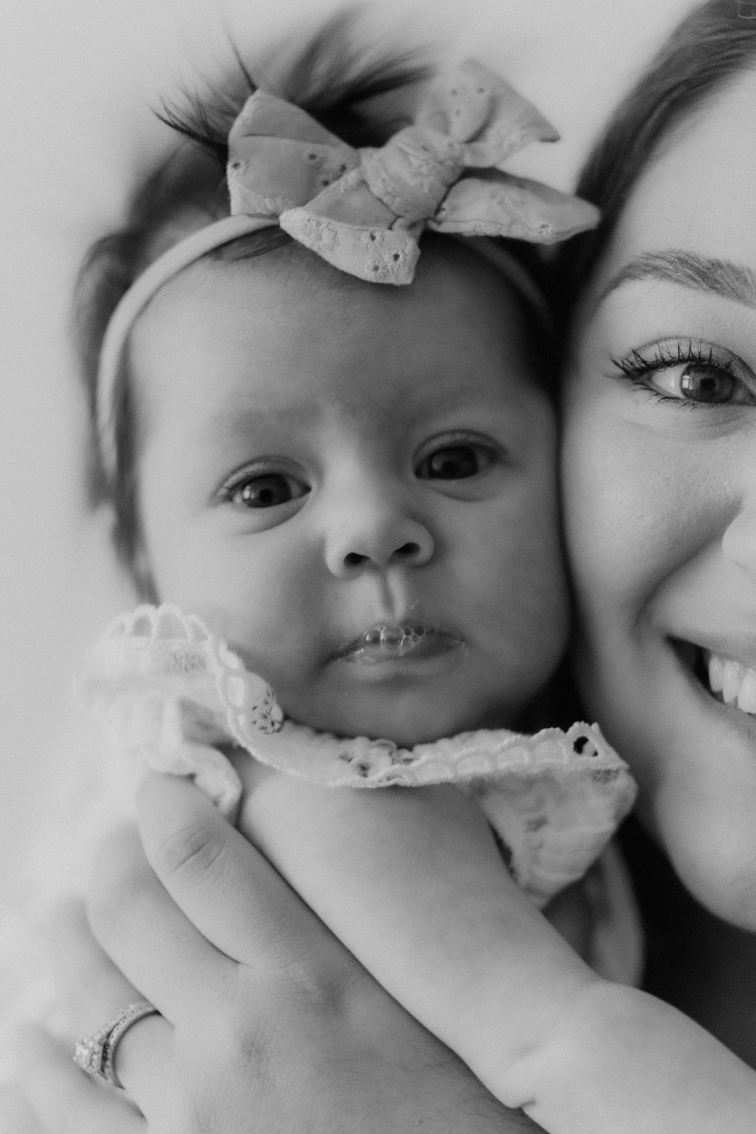 Black and white photo of smiling mother cheek to cheek with newborn baby girl.