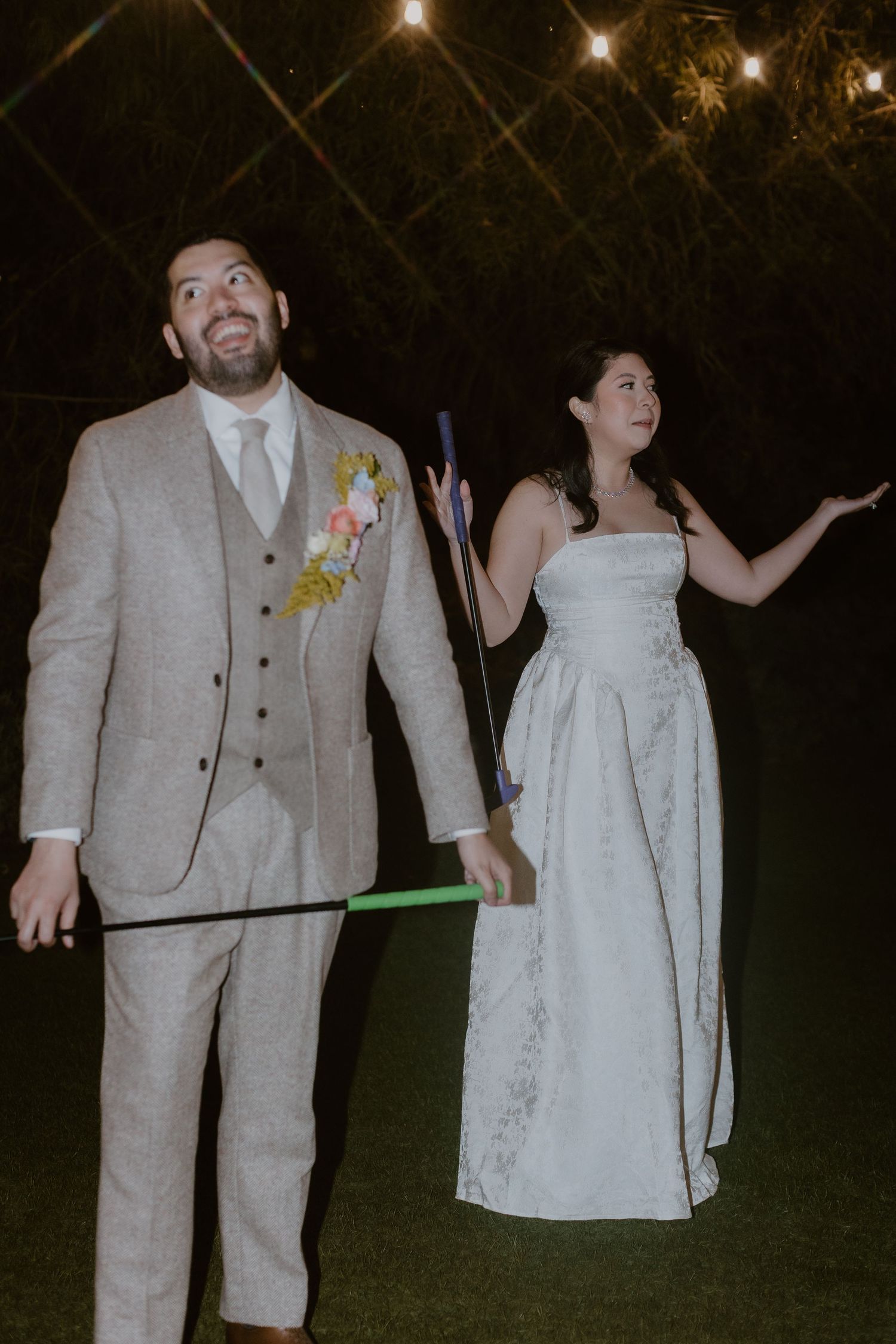 Bride and groom celebrating at night reception with colorful glow sticks under string lights.